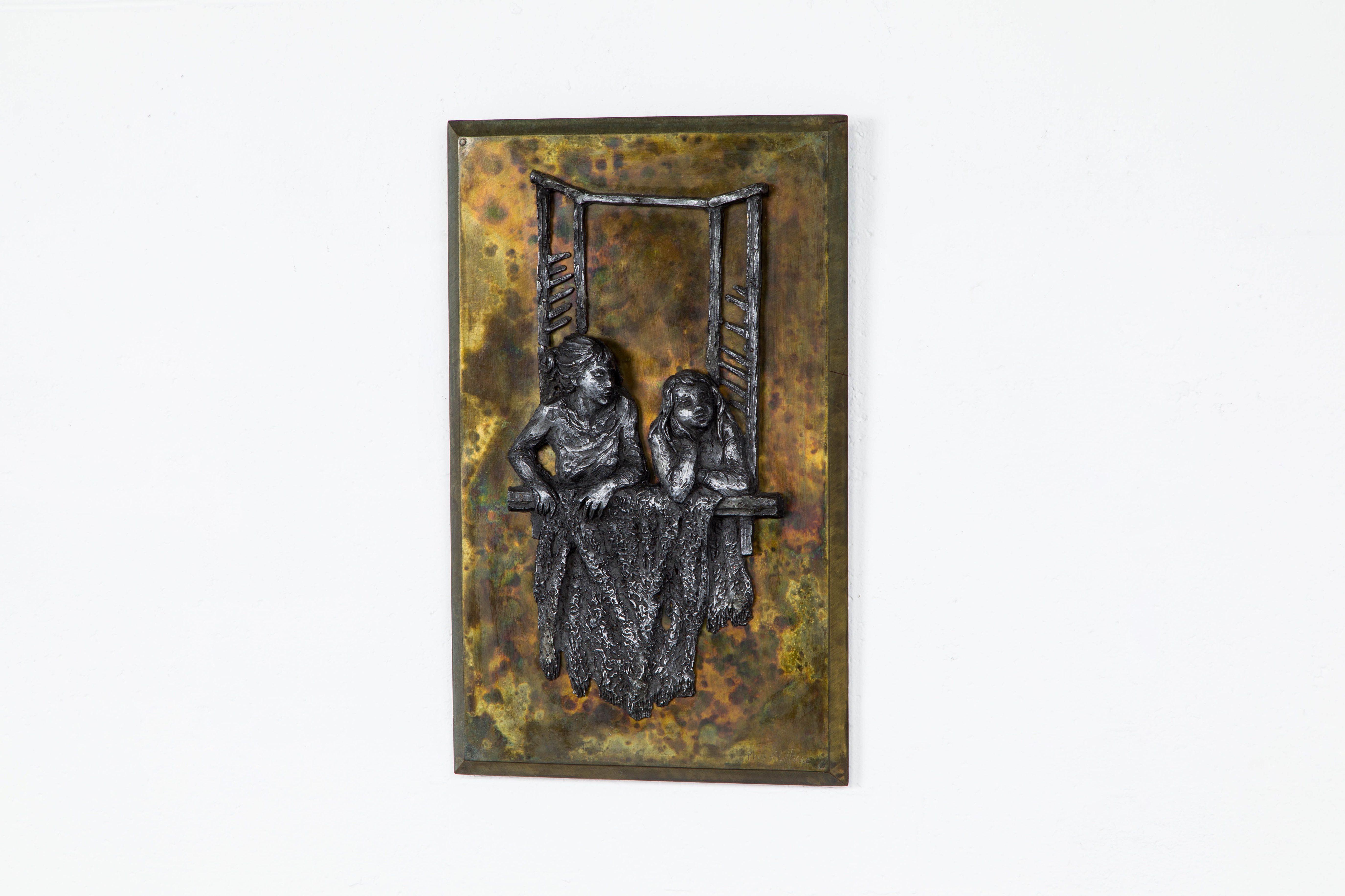 This work of fine art by Philip and Kelvin LaVerne (New York, 1960s) is a beautiful bronze and pewter wall relief which displays two young sisters leaning out of a latticed window frame holding a throw blanket. The relief was sculpted from pewter