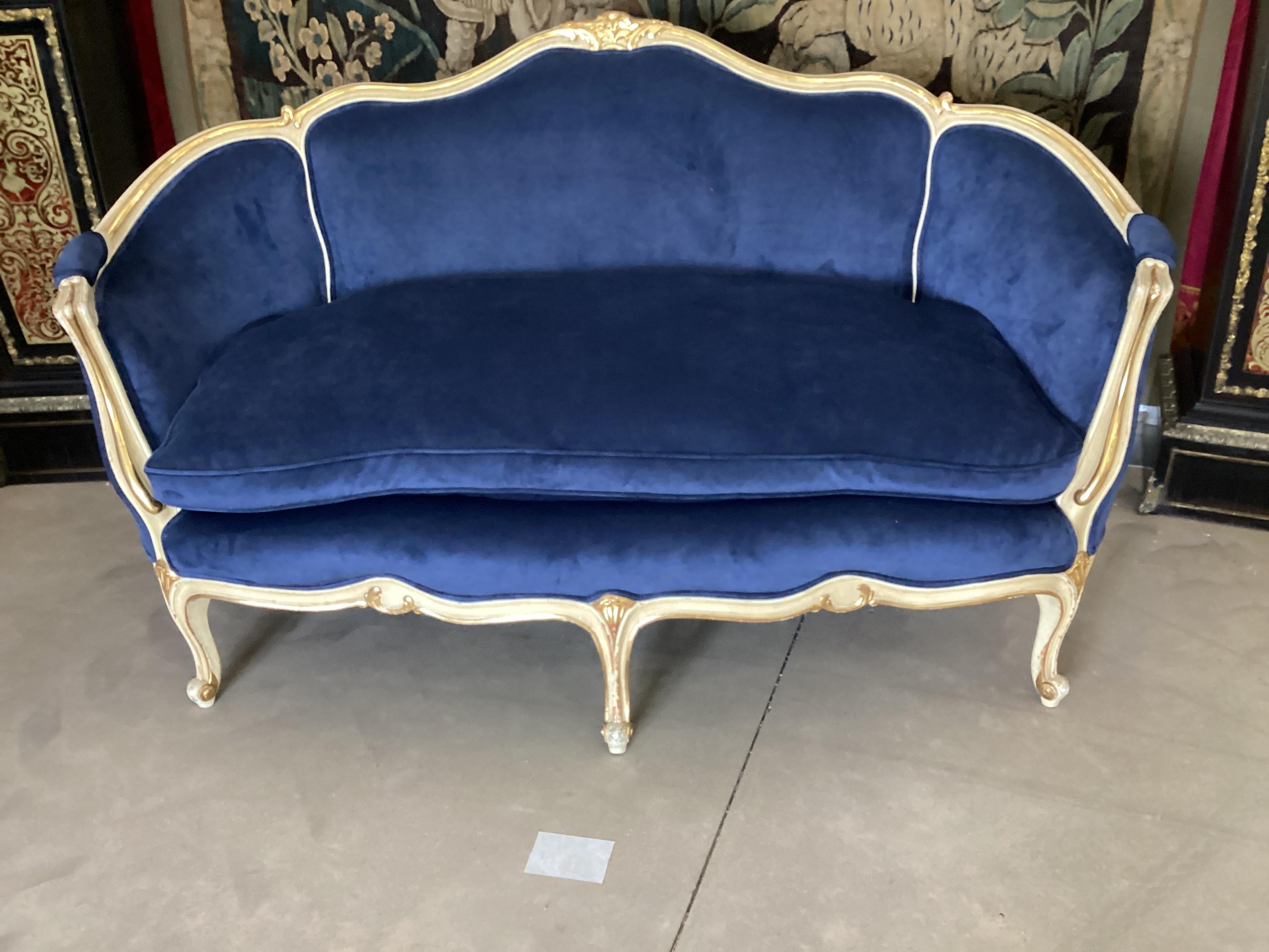 Antique Louis XV Style Painted and Gilt Settee. This is one of a pair and priced individually. Newly upholstered in a blue velvet fabric. Cream painted frame with gilt accents on typical 
Louis  XV  style scrolling legs. The pair would look great in