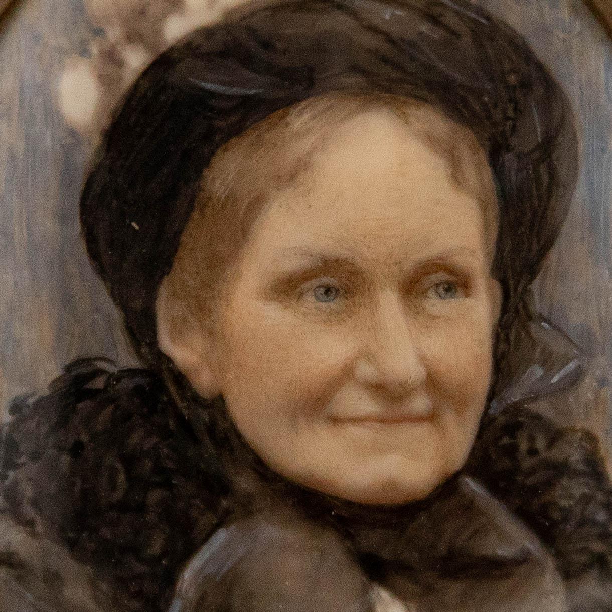 A charming miniature study of a Victorian woman dressed in a black ruffled dress and a hat. Presented in an oval brass frame. On a white bone-like substrate.