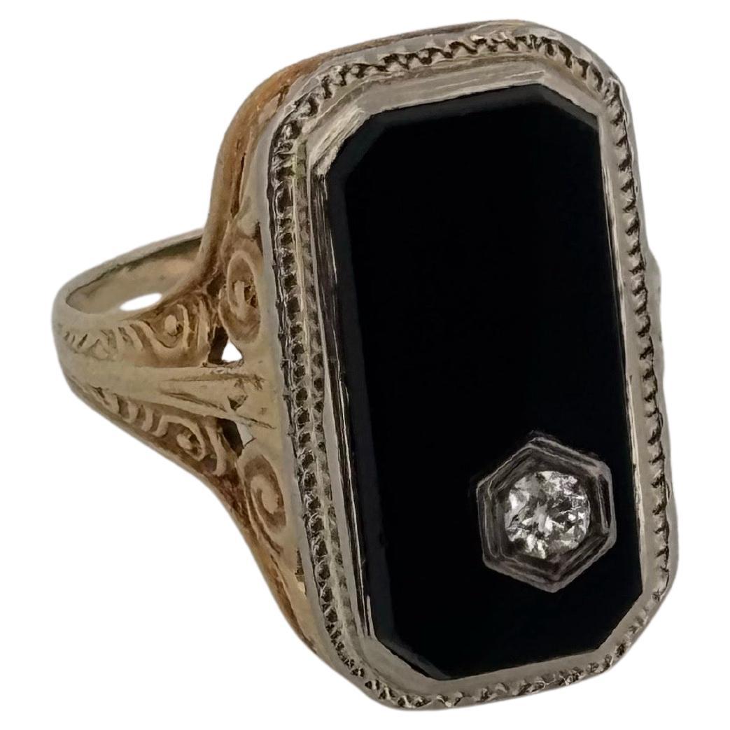Dieser antike Ring aus 14-karätigem Gelbgold, der mit einer Spitze aus Weißgold akzentuiert ist, ist ein raffiniertes Beispiel für die Handwerkskunst des frühen 20. Jahrhunderts. Das Herzstück ist ein hochglanzpolierter, rechteckiger schwarzer Onyx,