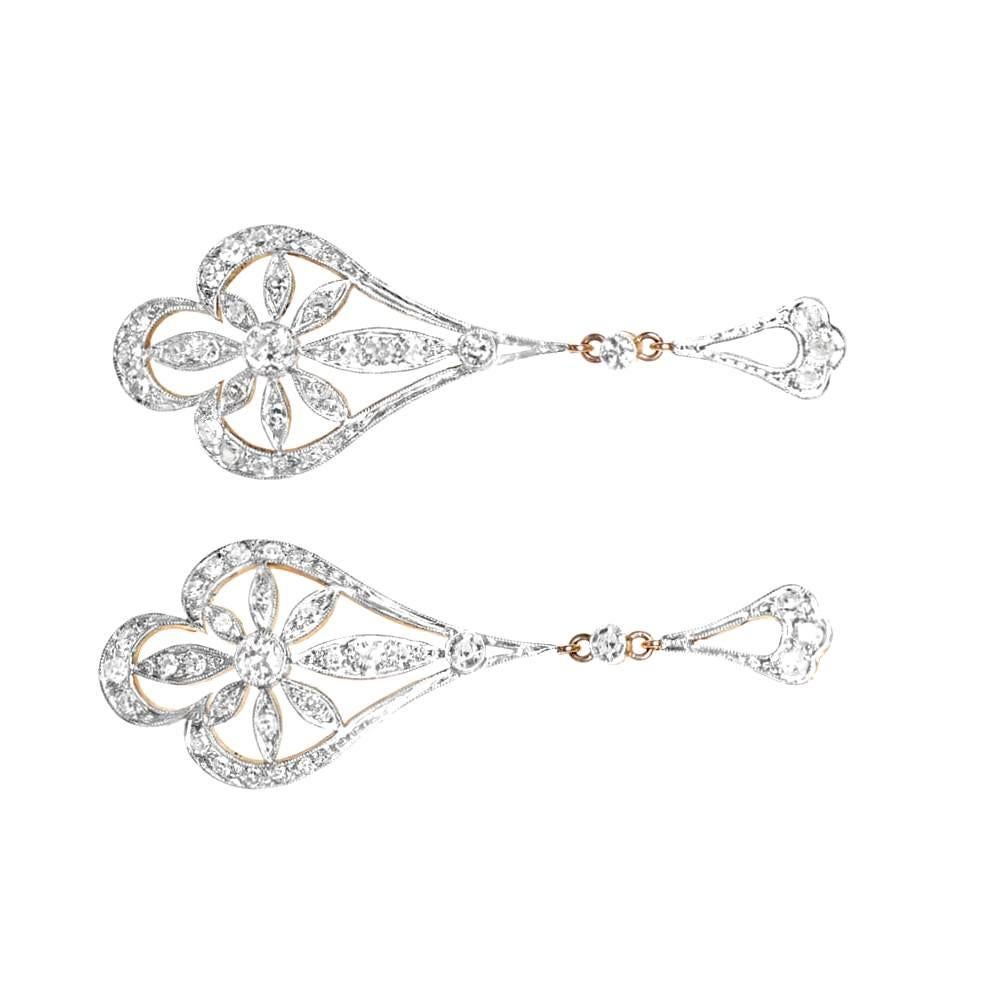 These exquisite Edwardian-style dangling earrings exude timeless elegance and intricate craftsmanship. Each earring features a pair of bezel-set transitional cut diamonds, approximately 0.12 carats each, gracefully taking center stage. Surrounding