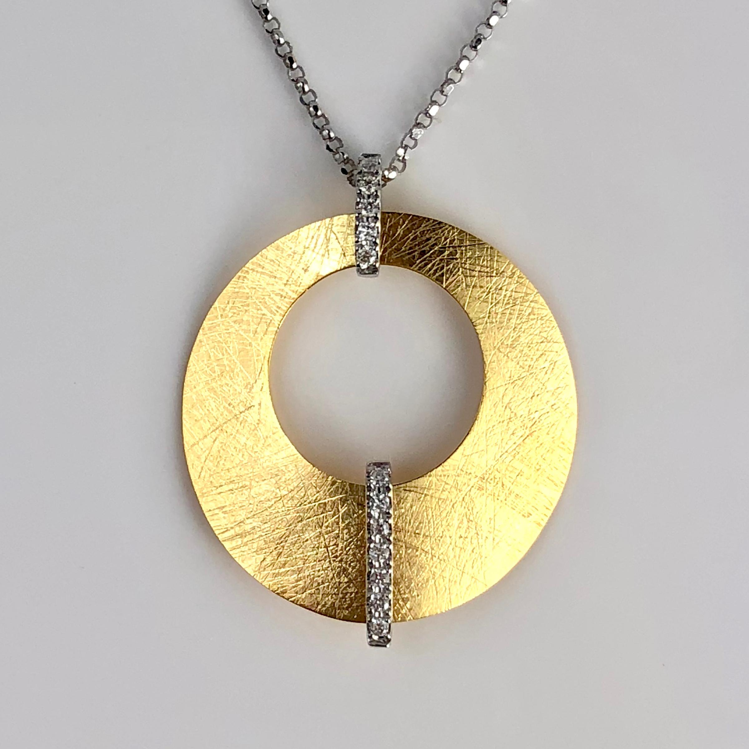This pendant is a round yellow gold disc with a round cutout. A line of diamonds crosses the top and bottom of the design. The total diamond weight is 0.13 carats.

Set in 14k Yellow and White Gold.

Many of our items have matching companion pieces.