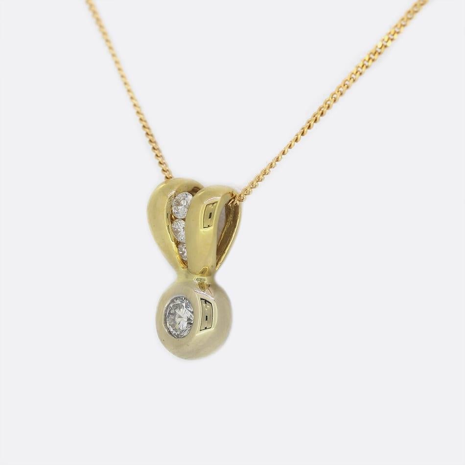 This is a single stone diamond pendant necklace. The pendant features a single round brilliant cut diamond that has been rubover set in 18ct yellow gold with a diamond set split bail and suspended on an 18ct yellow gold chain.

Condition: Used (Very
