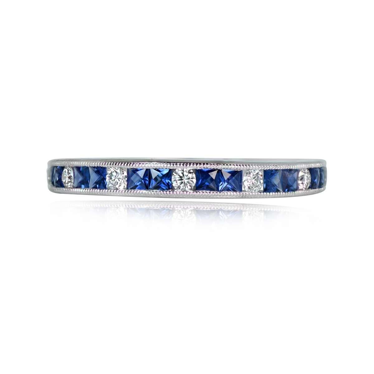 This exquisite half-eternity band is crafted in platinum, showcasing a captivating pattern of alternating round brilliant-cut diamonds and two natural blue French-cut sapphires. The stones are meticulously channel-set, and delicate milgrain