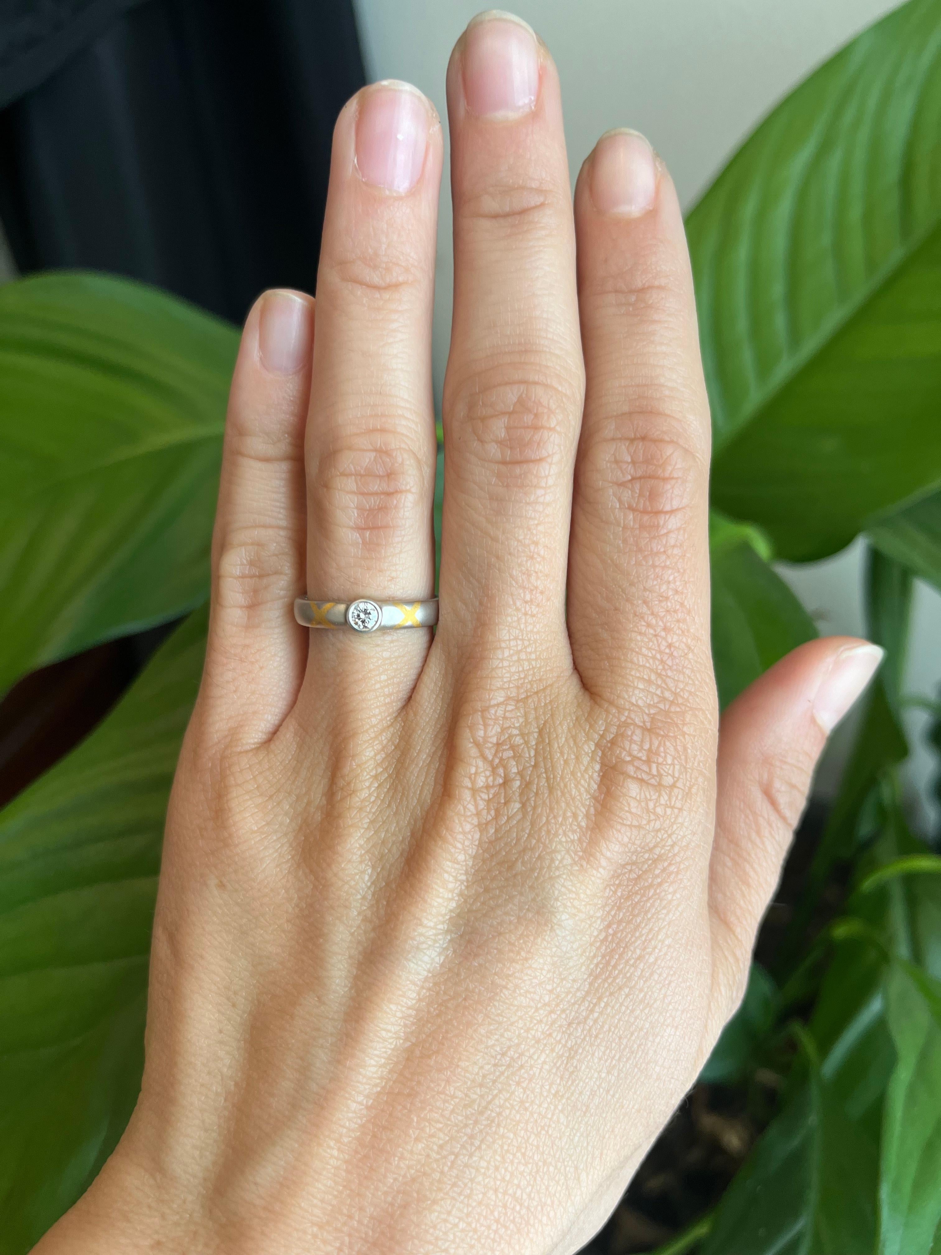 Ein zweifarbiger Solitär-Diamantring mit einem 0,15ct runden Naturdiamanten im Brillantschliff (Reinheit SI1, Farbe H). Der Stein ist tief in Platin gefasst, und das Band ist mit zwei 24-karätigen X verziert, die ein 