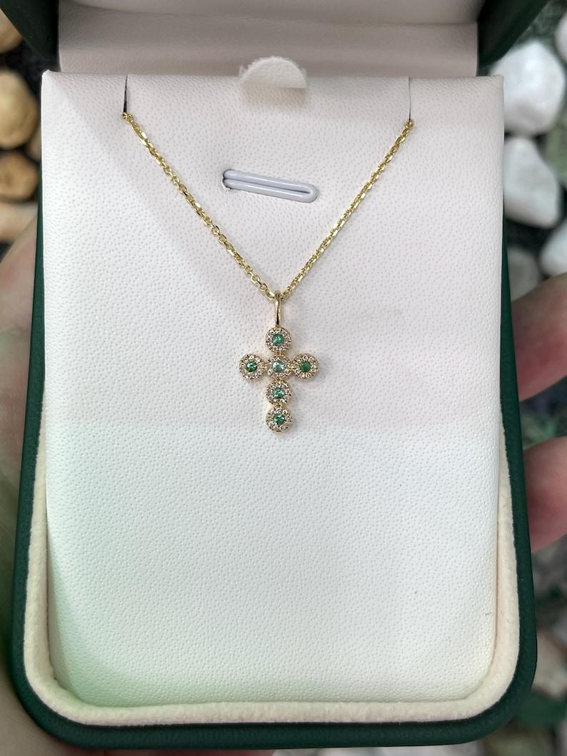 Questo squisito ciondolo a forma di mini croce è realizzato in oro 14 carati e presenta sei smeraldi di taglio rotondo, ciascuno incorniciato da un delicato alone di diamanti incastonati. Il suo design sottile lo rende perfetto per essere indossato