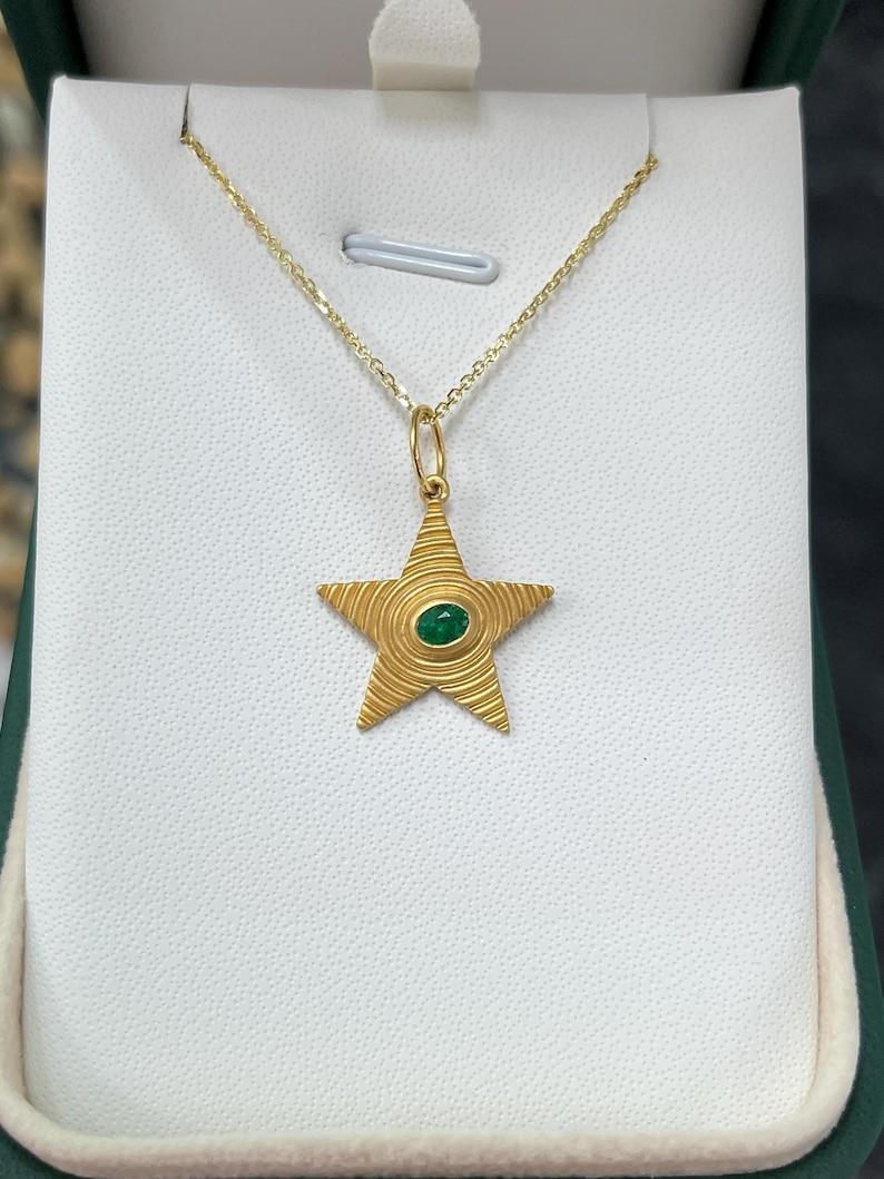 Découvrez la beauté éthérée de notre pendentif étoile d'émeraude, une pièce véritablement céleste centrée autour d'une émeraude ovale naturelle vert vif qui semble renfermer les mystères de l'univers. Fabriqué en or massif 14 carats, le motif ondulé