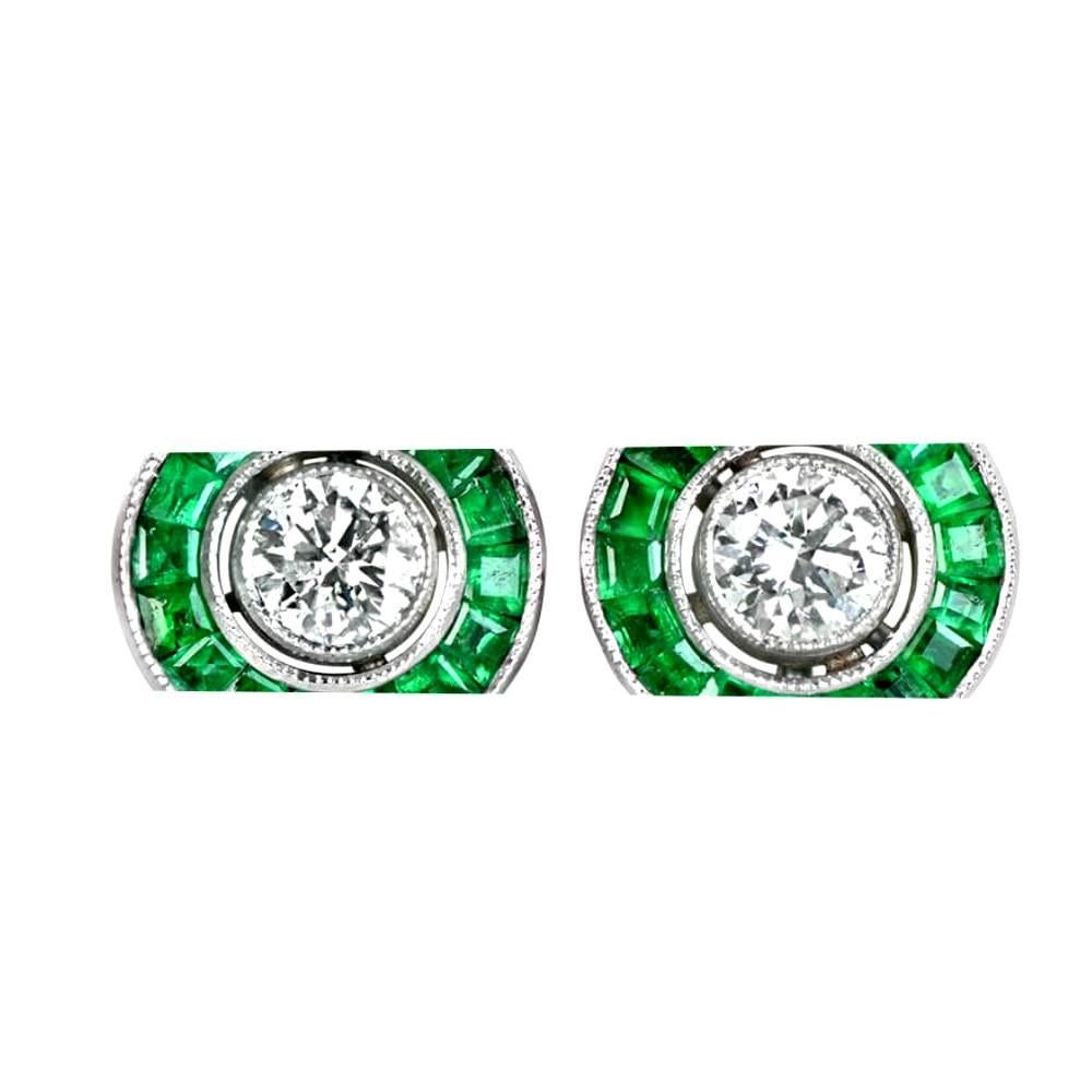 Indulge in the allure of these exquisite halo earrings, adorned with bezel-set round brilliant cut diamonds, each weighing around 0.20 carats. These dazzling center diamonds are embraced by halos of calibre cut natural green emeralds, totaling