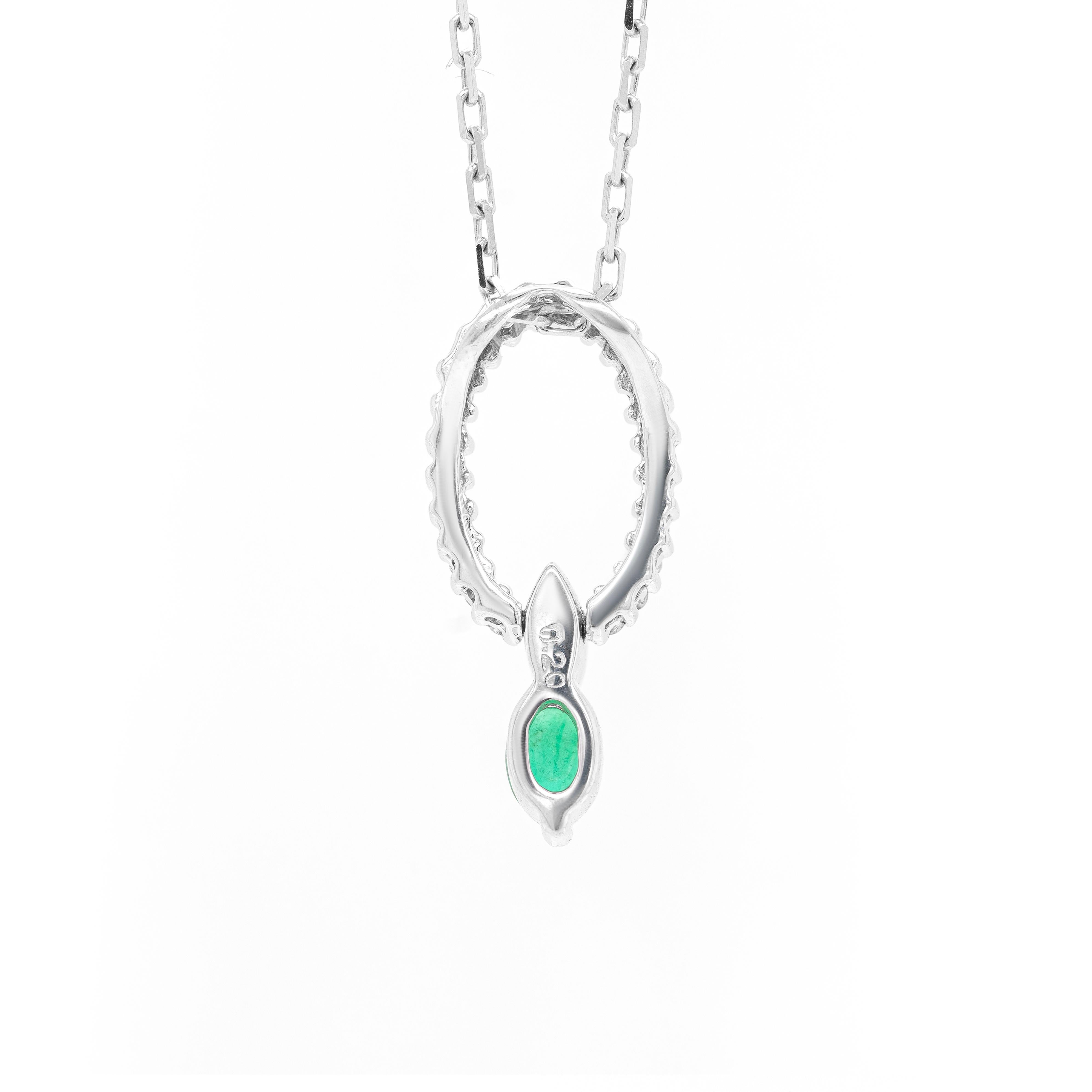 This delicate 18 carat white gold pendant is beautifully designed as an oval claw set with 23 fine quality round brilliant cut diamonds weighing 0.20ct in total. A vibrant oval shaped emerald weighing approximately 0.30ct suspends from the diamond