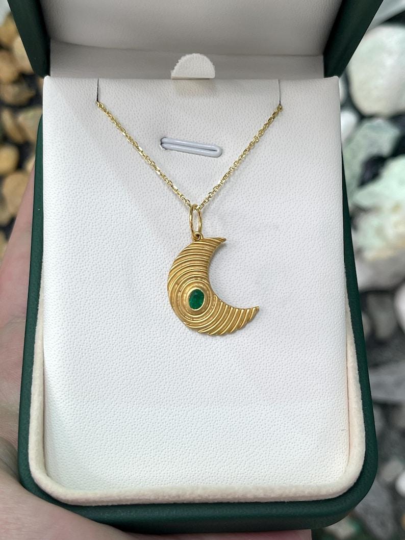 Laissez-vous séduire par l'allure mystique de notre pendentif croissant de lune en émeraude, une création éthérée composée d'une émeraude ovale captivante qui brille d'une teinte vert profond, comme un joyau cueilli dans le ciel nocturne. Sculpté