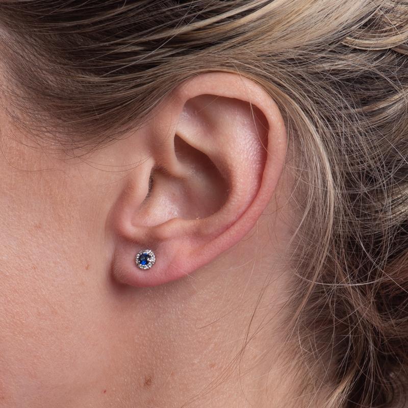 Ces boucles d'oreilles sont composées de saphirs naturels ronds bleus d'un poids total de 0,25 carat, rehaussés d'un halo de diamants d'un poids total de 0,07 carat, le tout serti dans de l'or blanc 14 carats. Poteau et dossier à friction.
