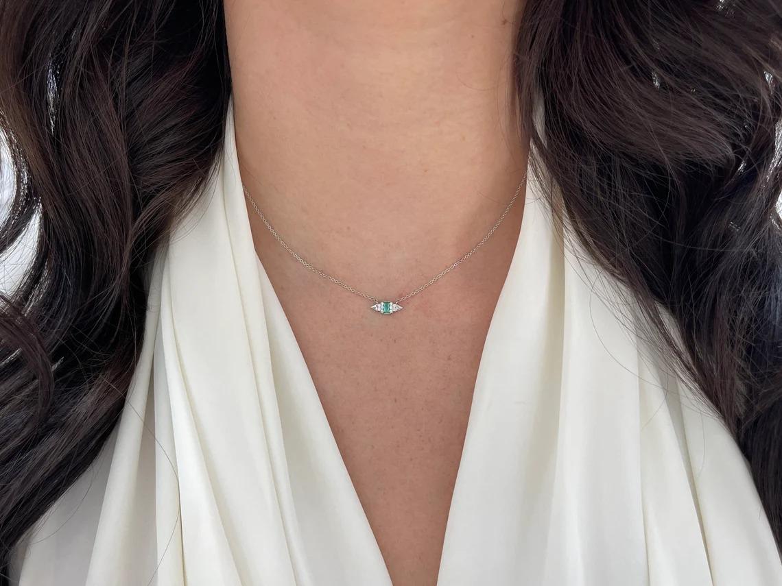 Featured here is a 0.20 carat stunning baguette cut emerald and round diamond accent petite pendant in 14K. Displayed in the center is a deep bluish-green emerald with incredible crystal clarity, accented by three round cut diamonds in a solid gold