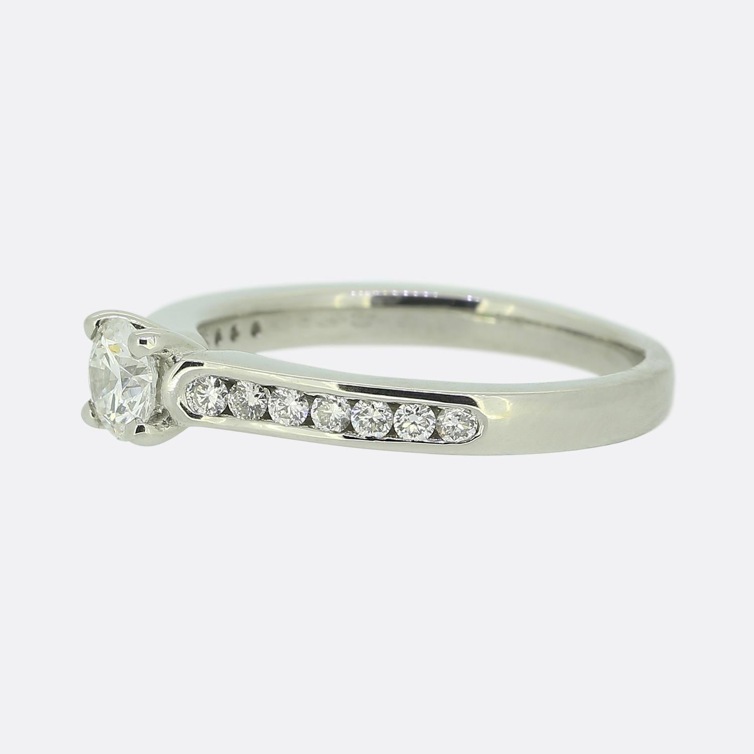 Hier haben wir einen diamantenen Verlobungsring aus Platin. Im Mittelpunkt dieses Schmuckstücks steht ein einzelner runder Diamant im Brillantschliff von 0,30 Karat, der stolz in der Mitte sitzt. Dieser Hauptstein wird durch sieben weitere Diamanten