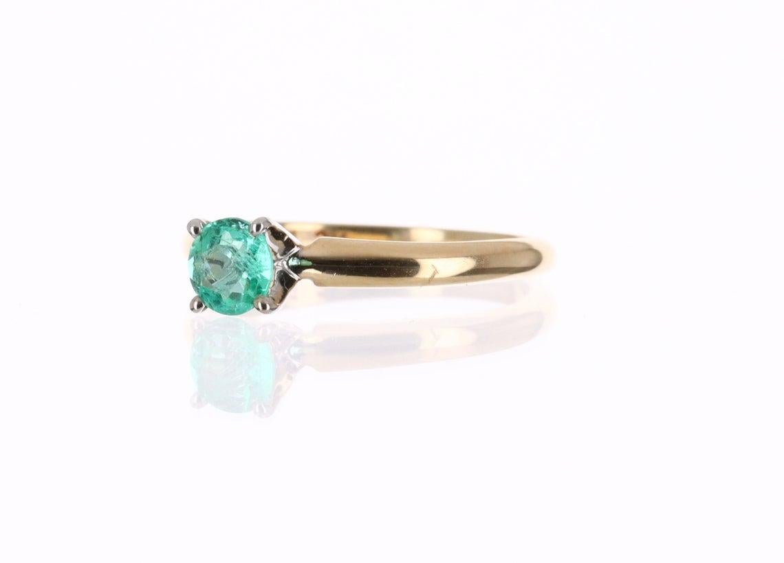 Displayed is a classic Colombian emerald solitaire, round-cut, engagement ring in 14K yellow gold. This gorgeous solitaire ring carries a full 0.30-carat emerald in a four-prong setting. Fully faceted, this gemstone showcases excellent shine. The