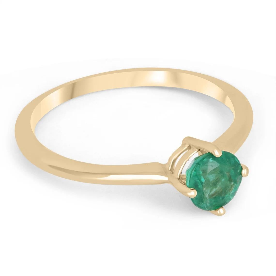 Displayed is a classic emerald solitaire, round-cut, engagement ring in 14K yellow gold. This gorgeous solitaire ring carries a full 0.30-carat emerald in a four-prong setting. Fully faceted, this gemstone showcases excellent shine. The emerald has