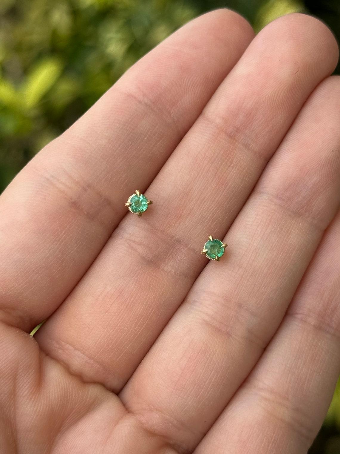 Eleva tu elegancia cotidiana con nuestros encantadores pendientes pequeños, con dos esmeraldas de talla redonda de 0,30 quilates, cada una delicadamente engarzada en un seguro soporte de cuatro garras de oro de 14 quilates. Elaborados con sutil
