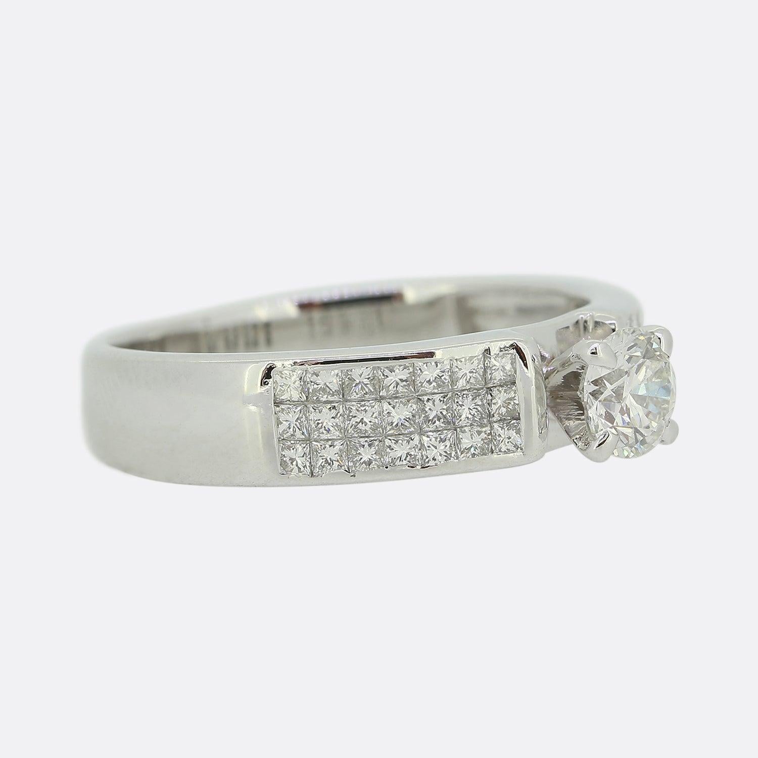 Hier haben wir einen diamantenen Verlobungsring aus 18 Karat Weißgold. Dieser Solitär ist mit einem einzelnen runden Diamanten im Brillantschliff in der Mitte und einer Reihe von pavégefassten Diamanten im Prinzessschliff auf beiden Schultern