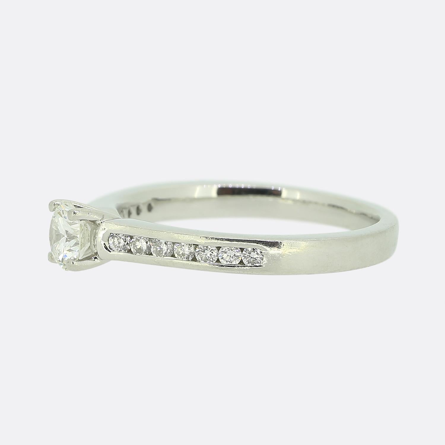 This is a lovely platinum diamond engagement ring. The focal point of this ring is a 0.32 carat round brilliant cut diamond which sits proud at the centre of the face whilst being flanked on either shoulder by a single row of seven channel set