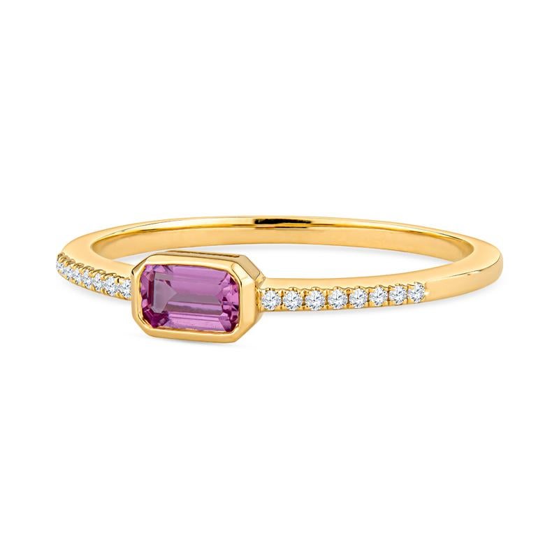 This dainty ring features an emerald cut pink sapphire set east-west accented by 0.05 carat total weight in round diamonds on the band set in 14 karat yellow gold. It is a size 6.5 but can be resized upon request. This ring can be worn alone or