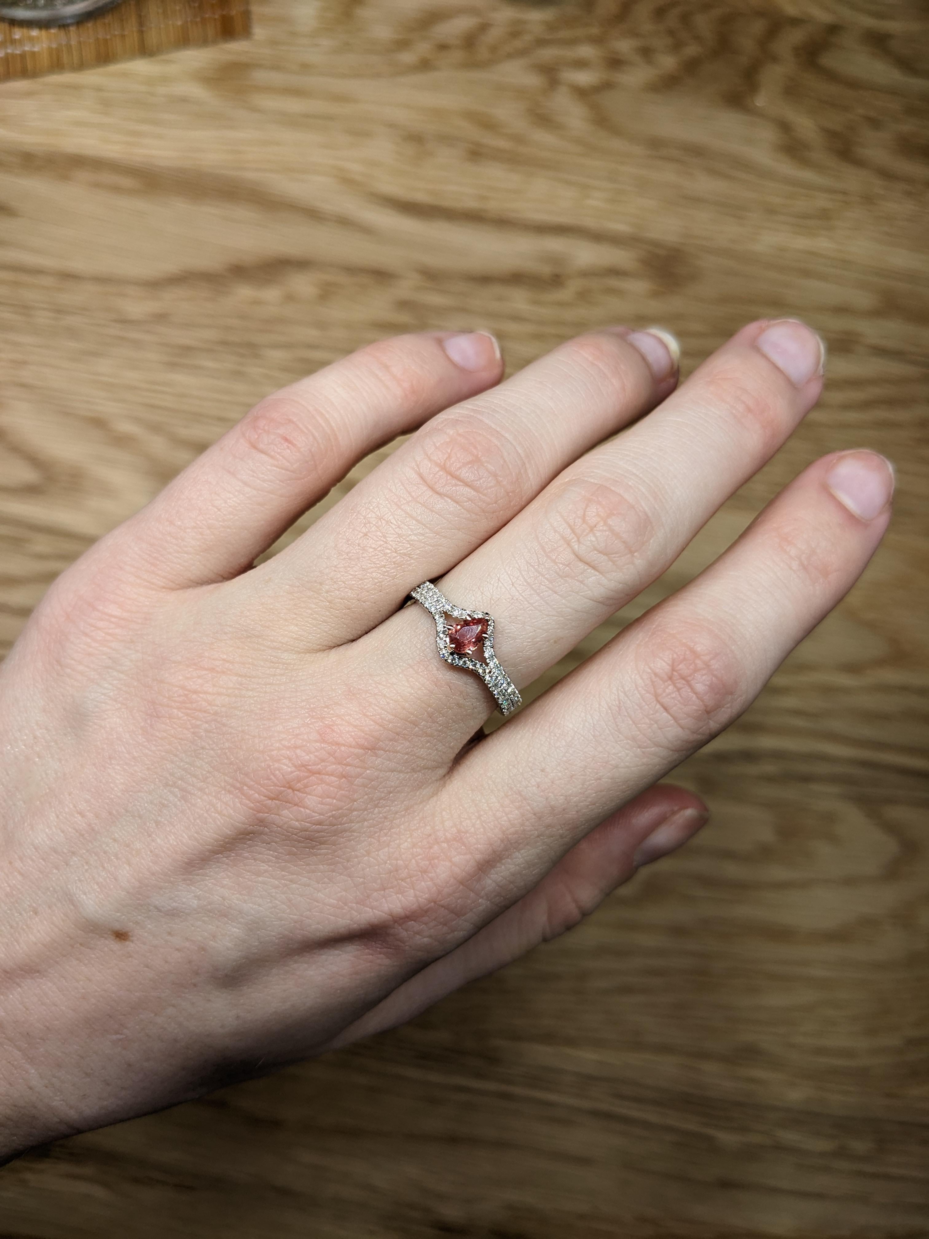 An elegant engagement ring features a stunning 0.33-carat Padparadscha sapphire in a captivating pear shape (6x4mm). Known for its rare and unique blend of pink and orange hues, the Padparadscha sapphire sits delicately at the center, surrounded by