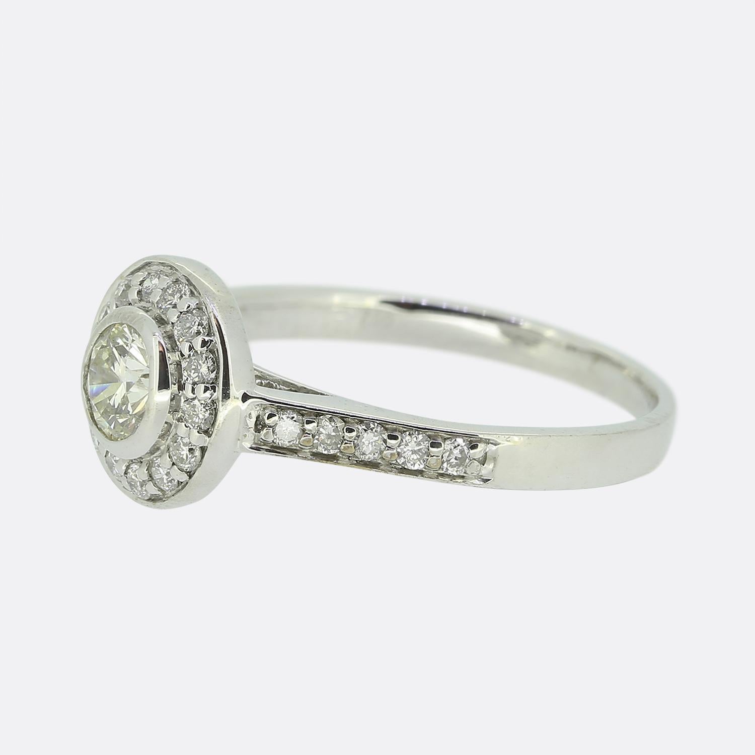 Qui abbiamo un anello con diamante aureolato in oro bianco 18ct. Un singolo diamante rotondo taglio brillante è stato incastonato al centro del quadrante ed è circondato da un'unica fila di 14 diamanti più piccoli lungo il bordo esterno. L'anello è