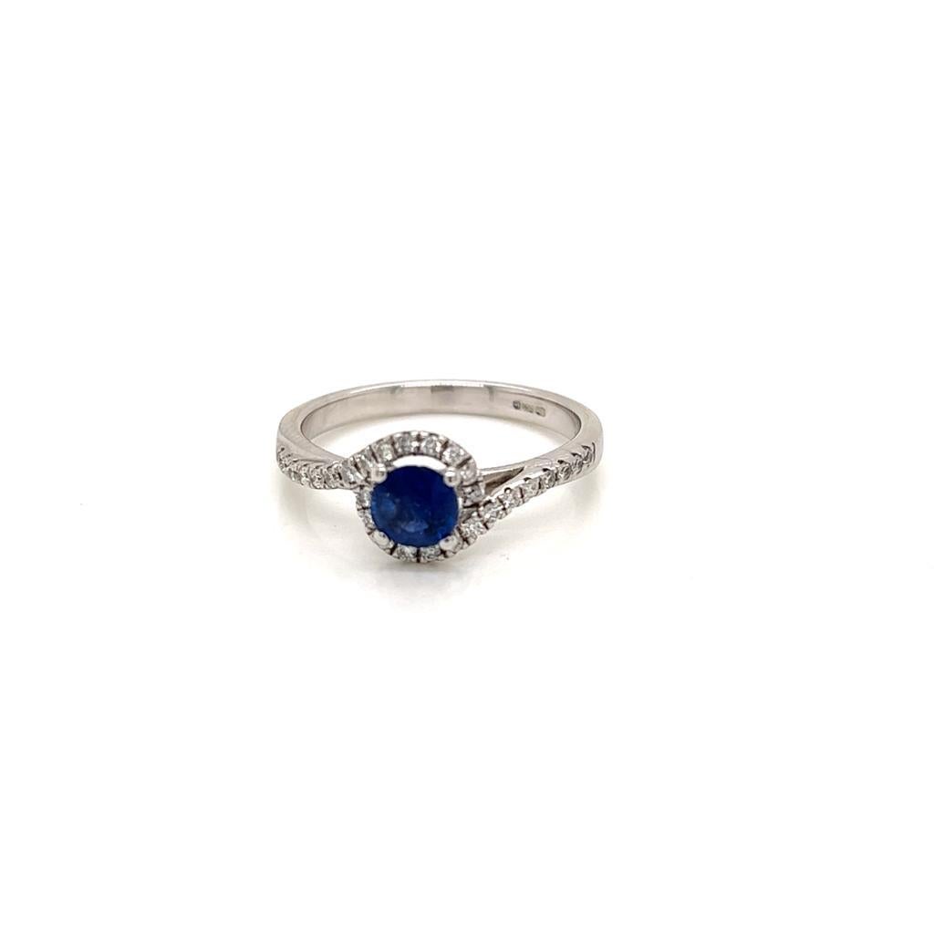 This Dainty Ring features a breath-taking Round Brilliant Blue Sapphire weighing approximately 0.35 carats which is surrounded by  Gleaming Diamonds weighing approximately 0.22 carats that extend to the 18K White Gold band. This Sophisticated