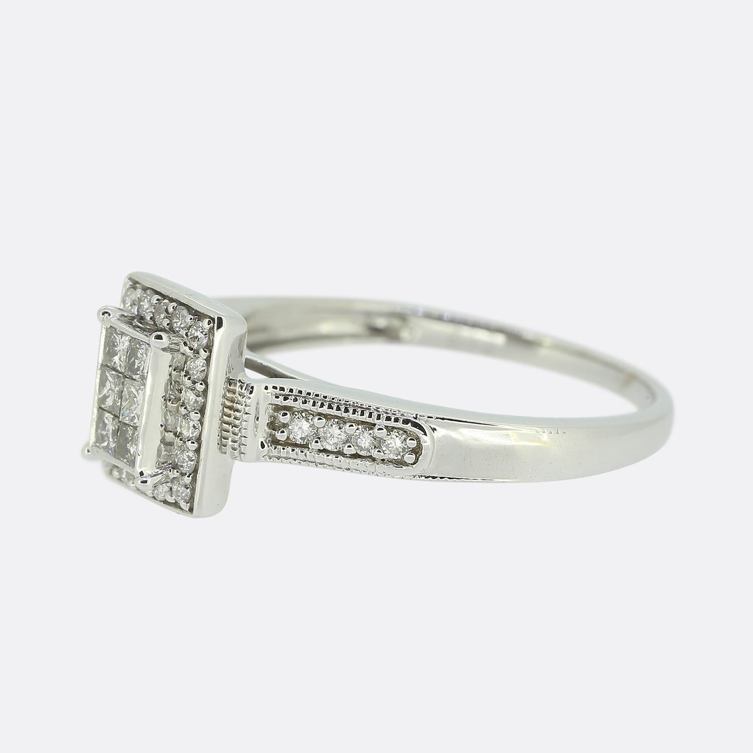 Hier haben wir einen Diamant-Cluster-Ring aus 18 Karat Weißgold. Die Vorderseite dieses Rings ist rechteckig und mit 6 Diamanten im Prinzessinnenschliff und 18 runden Diamanten im Brillantschliff besetzt. Auf jeder Schulter befinden sich weitere 4