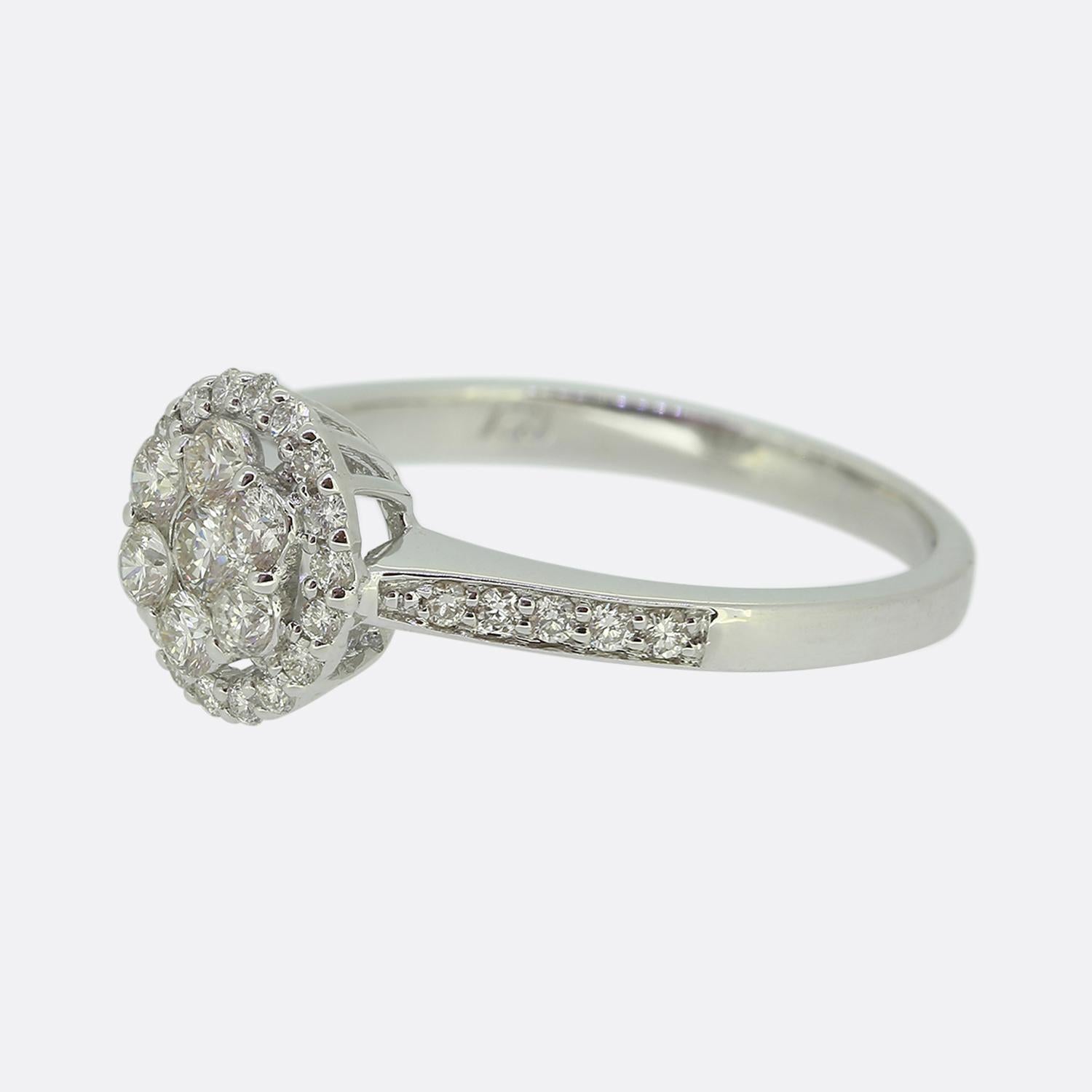 Hier haben wir einen klassisch gestylten Diamant-Cluster-Ring. In der Mitte befindet sich ein einzelner runder Diamant im Brillantschliff, der von sechs weiteren, etwas kleineren, passenden Steinen umgeben ist. Dieser Cluster erhebt sich inmitten