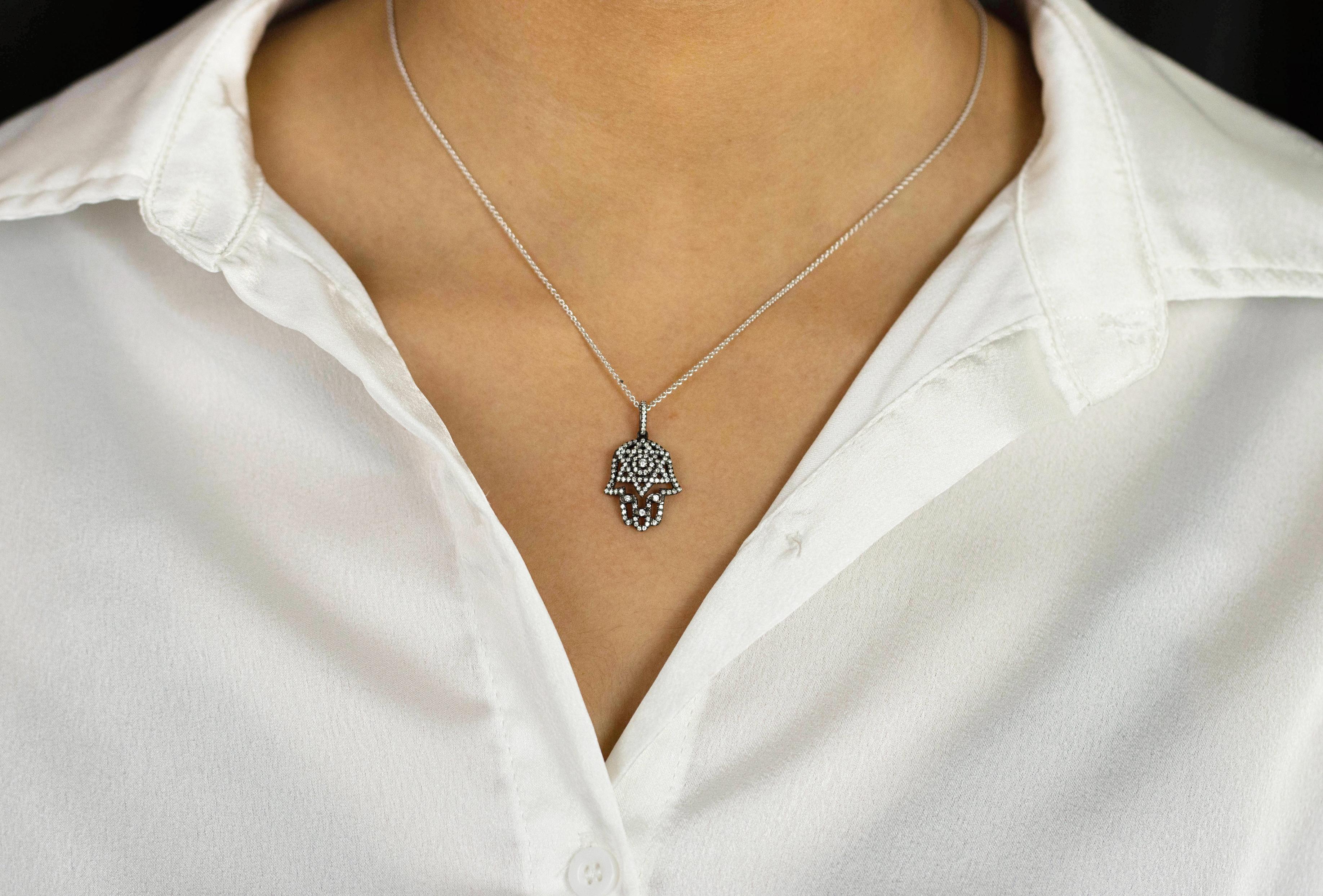 A hamsa pendant necklace showcasing a hand with a six-point star in the middle, encrusted with round brilliant diamonds. Attached to an diamond encrusted bale. Diamonds weigh 0.40 carats total. Black rhodium-plated and attached to a 16 inches