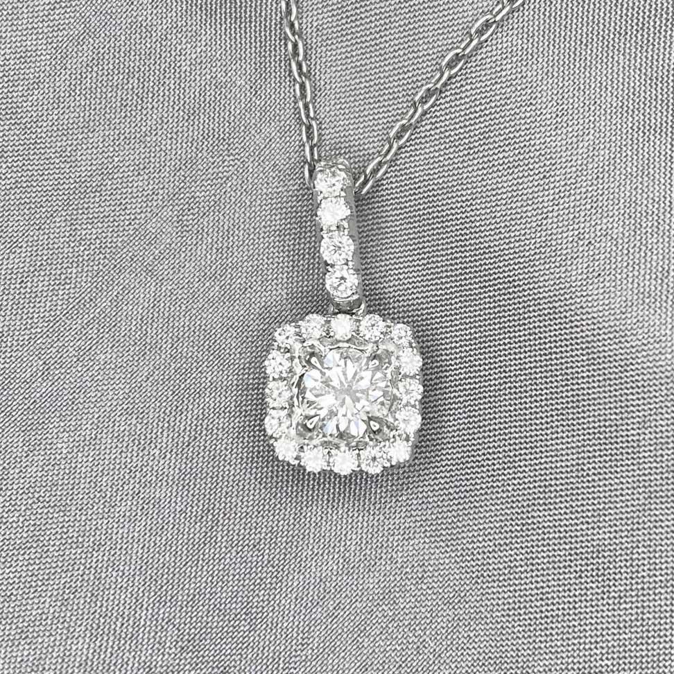 Radiating elegance, this pendant showcases a round brilliant cut diamond of around 0.40 carats, nestled securely in prongs. A captivating halo of diamonds encircles the center stone, while additional diamonds adorn the loop and back of the pendant.