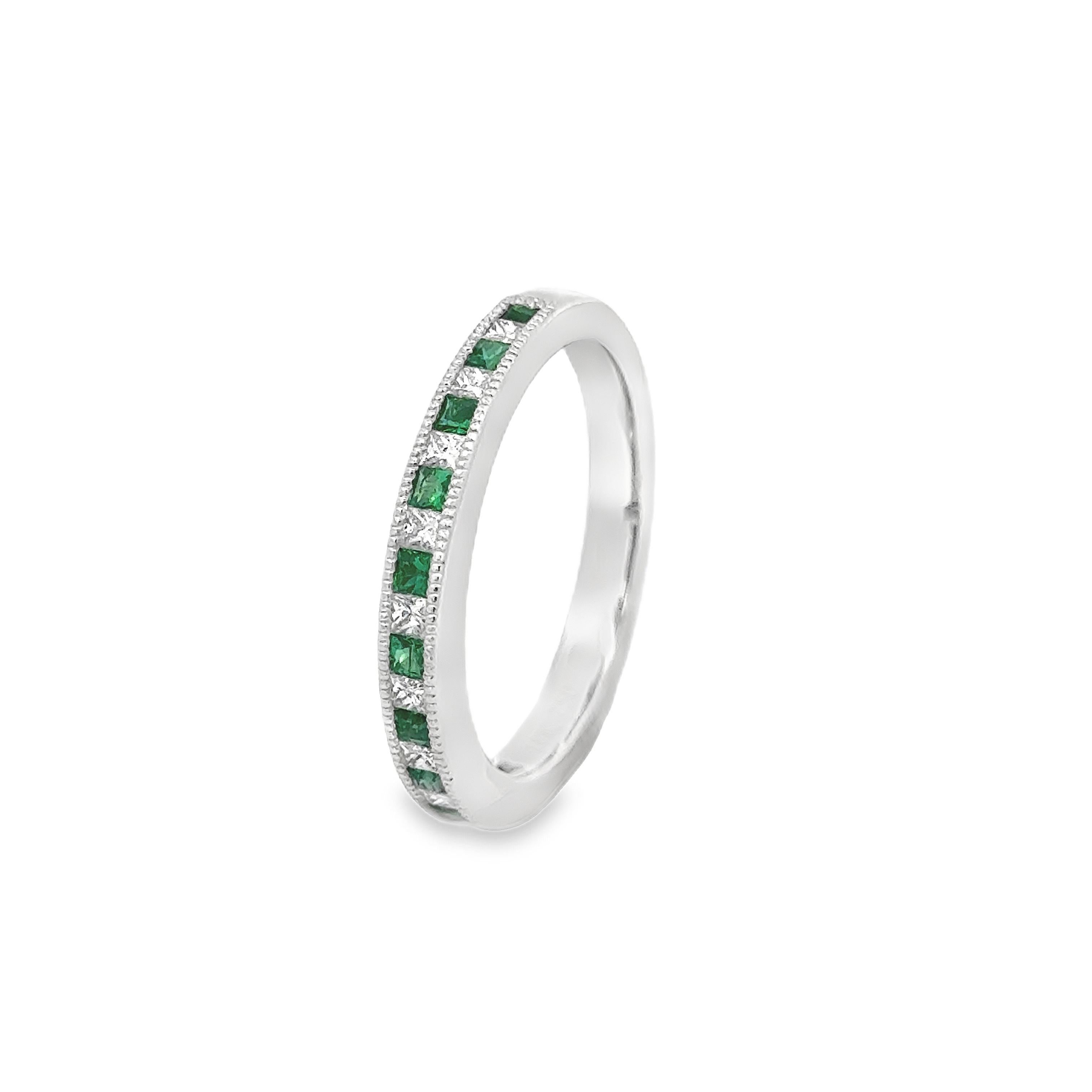 A fashionable semi-eternity wedding band ring, featuring eleven princess cut emeralds weighing 0.23 carat total and ten princess cut diamonds weighing 0.20 carat total, channel-set in an alternating fashion and finished with milgrain edges. Finely