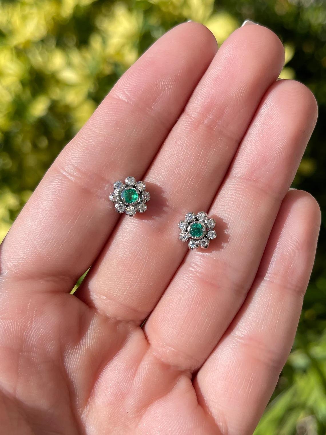 A beautiful pair of emerald and diamond stud earrings. The center stone features a round-cut, Colombian emerald with superb qualities. Surrounding the center stone are eight brilliant round cut diamonds creating the perfect halo effect. Carefully
