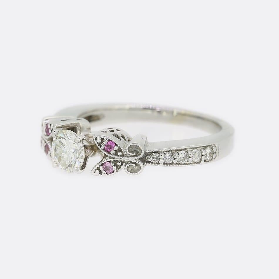 Si tratta di un anello solitario con diamante in oro bianco 18 ct. Il punto focale dell'anello è un diamante rotondo taglio brillante da 0,45 carati. Su ogni spalla c'è un elegante disegno che ospita due zaffiri rosa e altri 5 diamanti su ogni lato