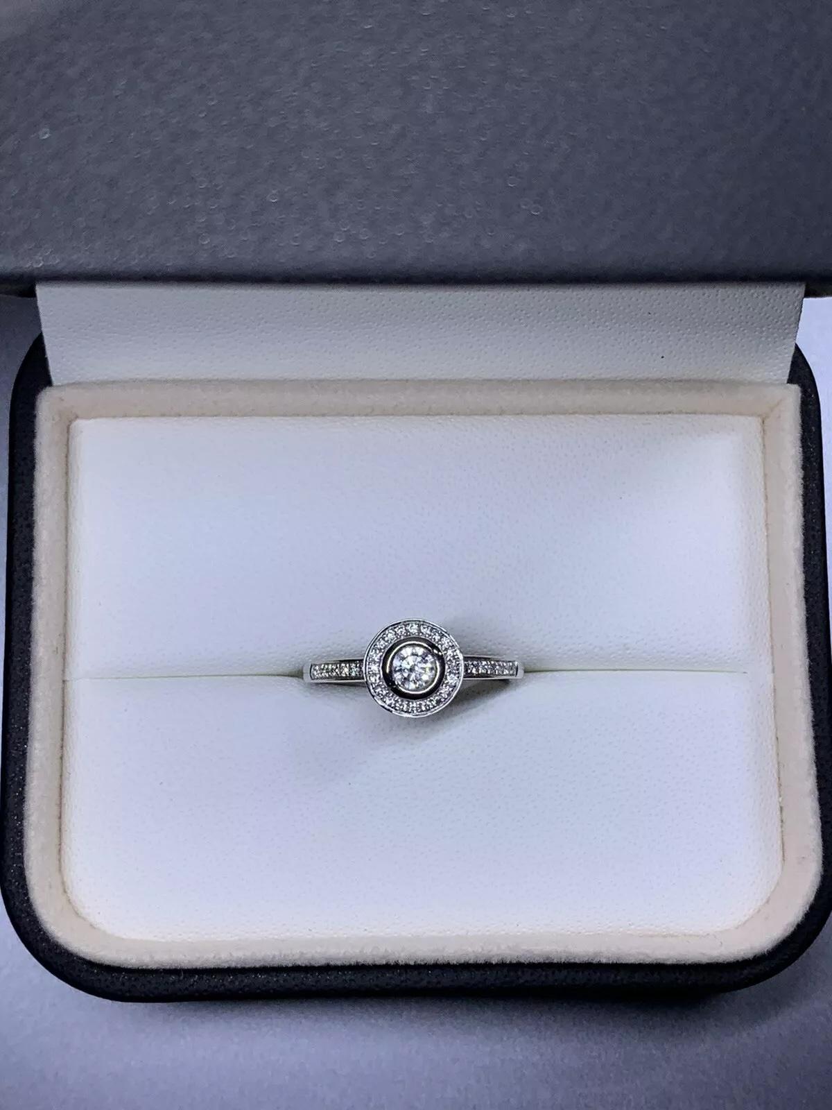 This beautiful ring features a stunning solitaire halo design with a total carat weight of 0.45ct. The main stone is a natural round diamond with an excellent cut grade and a G colour grade. The diamond is set in 18ct white gold with a band width of
