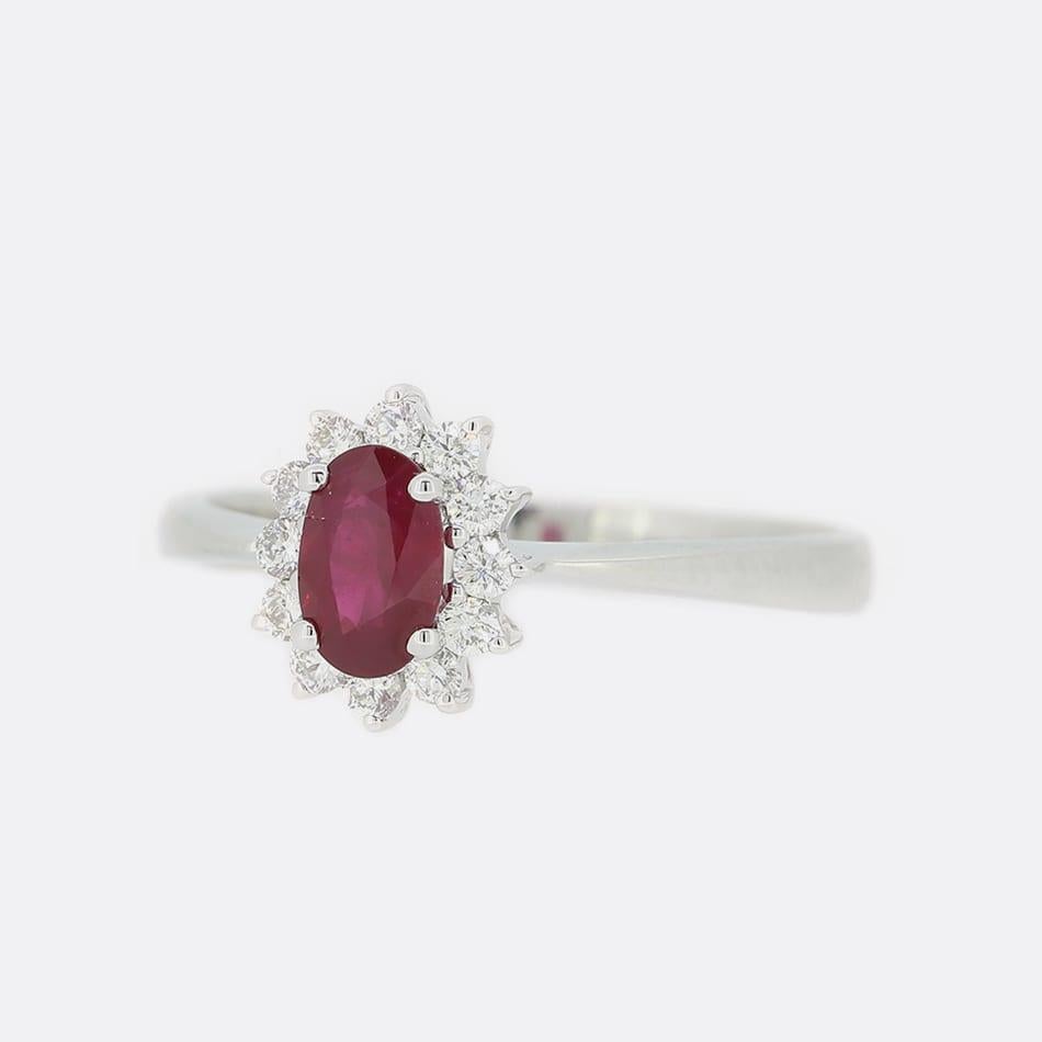 This is an 18ct white gold ruby and diamond ring. It features a single oval cut ruby surrounded by a cluster of 12 bright white brilliant cut diamonds which have been claw set in a white gold setting.

Condition: Used (Excellent)
Weight: 2.7