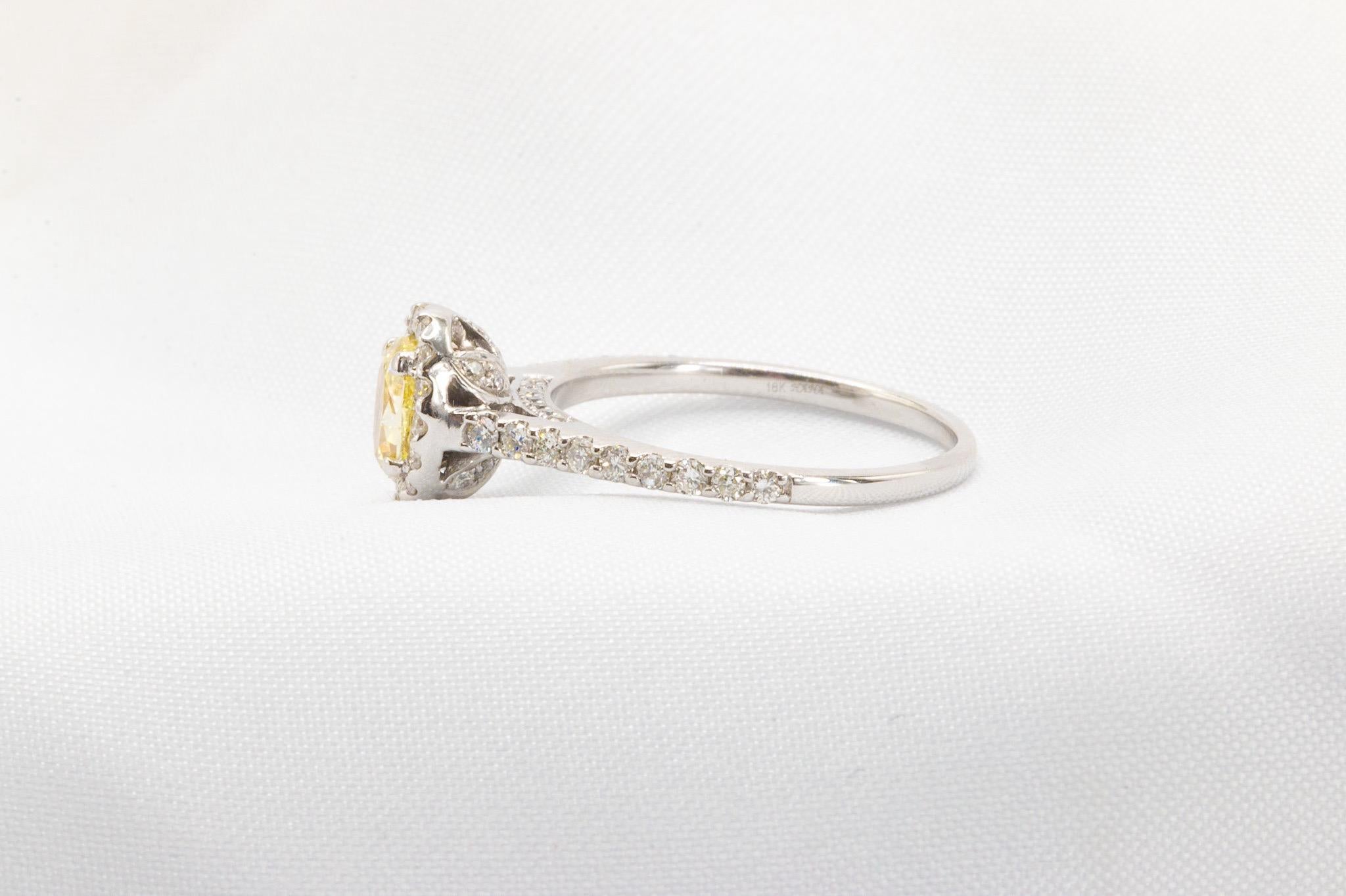 Crafted in 18K white gold, this elegant ring features an estimated total diamond weight of 1 carat. At its center is a stunning 0.50-carat oval yellow diamond with SI2-I1 clarity, beautifully accentuated by a halo of round brilliant diamonds that