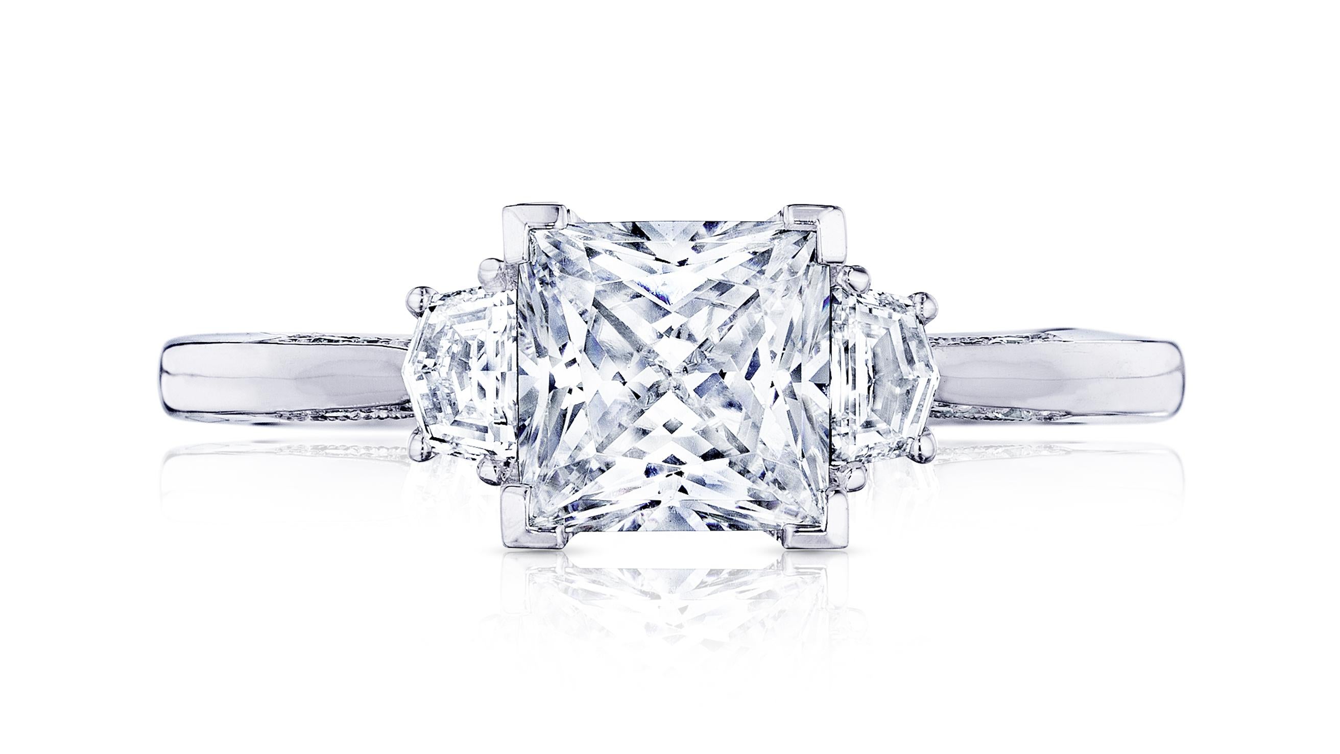 An exceptional engagement ring and sparkling precious jewel, features a round brilliant diamond center stone, given prominence by two tapered trapezoid side stones on a delicate platinum band. The delicate details of this refined diamond jewelry