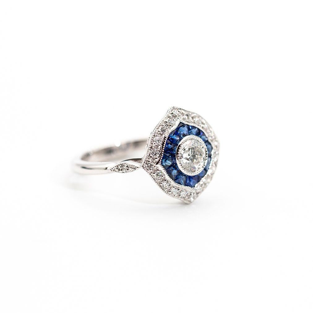 This romantic ring is forged in 18 carat white gold and adorns a central bright 0.50 carat certified round brilliant cut diamond surrounded by an alluring border of natural blue custom cut sapphires and 0.21 carats of round brilliant cut diamonds.
