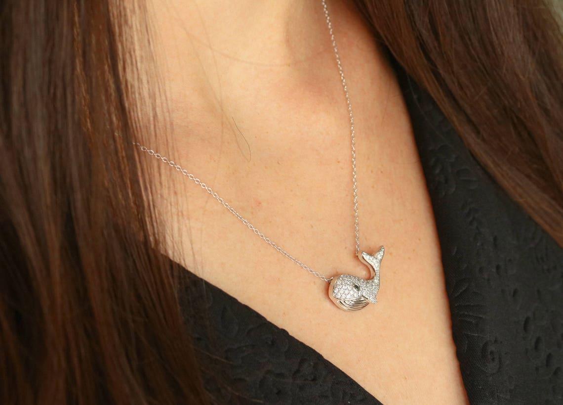 Displayed is a romantic diamond and sapphire whale necklace. The beautiful piece features numerous pave set diamonds that follow the curves of the whale and a bezel set sapphire that represents the eye. Smooth, engraved detail can be seen on the