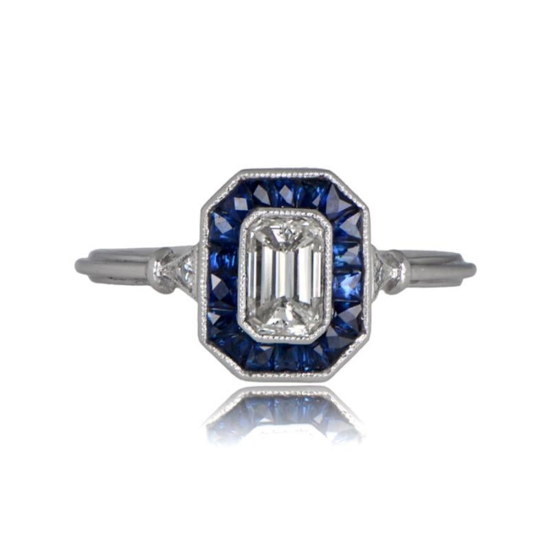 This exquisite platinum engagement ring showcases a bezel-set emerald-cut diamond, weighing around 0.52 carats, with a J color grade and VS1 clarity. The diamond is elegantly encircled by a halo of French-cut sapphires, totaling approximately 0.66