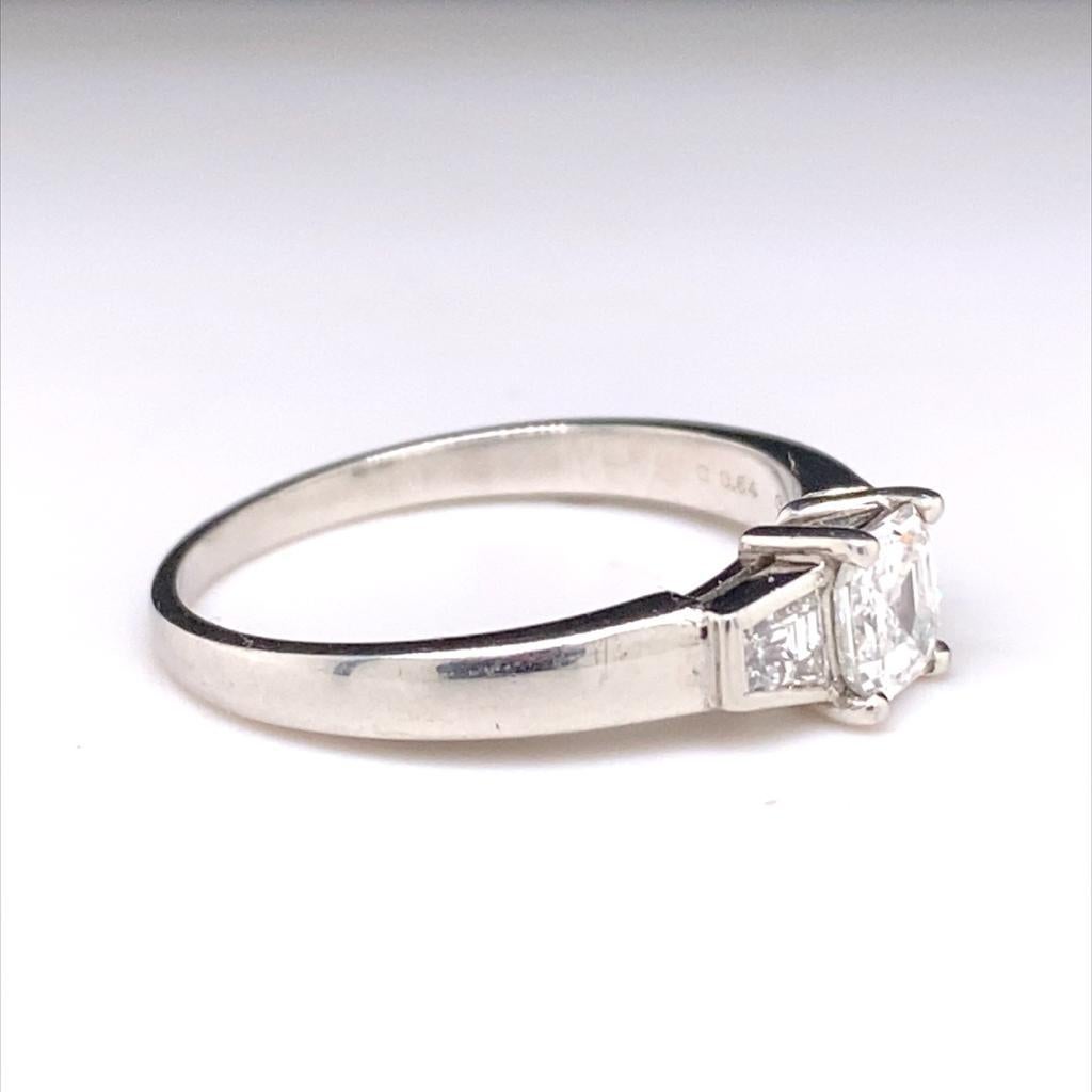 Ein 0,54 Karat schwerer Verlobungsring aus Platin mit drei Diamanten im Asscher-Schliff.

Dieser klassische Ring ist mit einem Diamanten im Asscher-Schliff besetzt und wird von einem weiteren spitz zulaufenden quadratischen Diamanten auf beiden