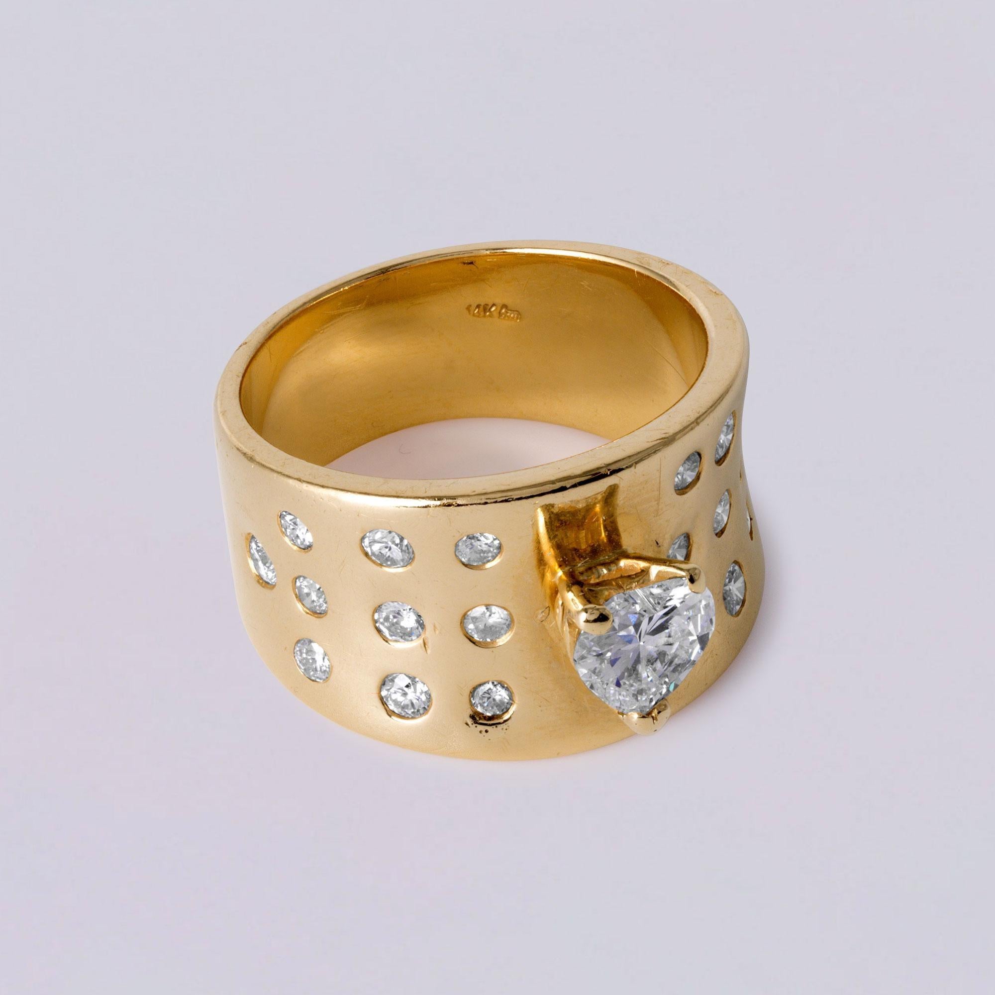 Dieses kühne und luxuriöse, ultrabreite Goldband mit einem auffälligen herzförmigen Diamanten von 0,55 Karat in der Mitte ist ein selbstbewusstes und romantisches Statement. Um das Herz herum sind 20 runde Brillanten von insgesamt ca. 0,75 Karat in