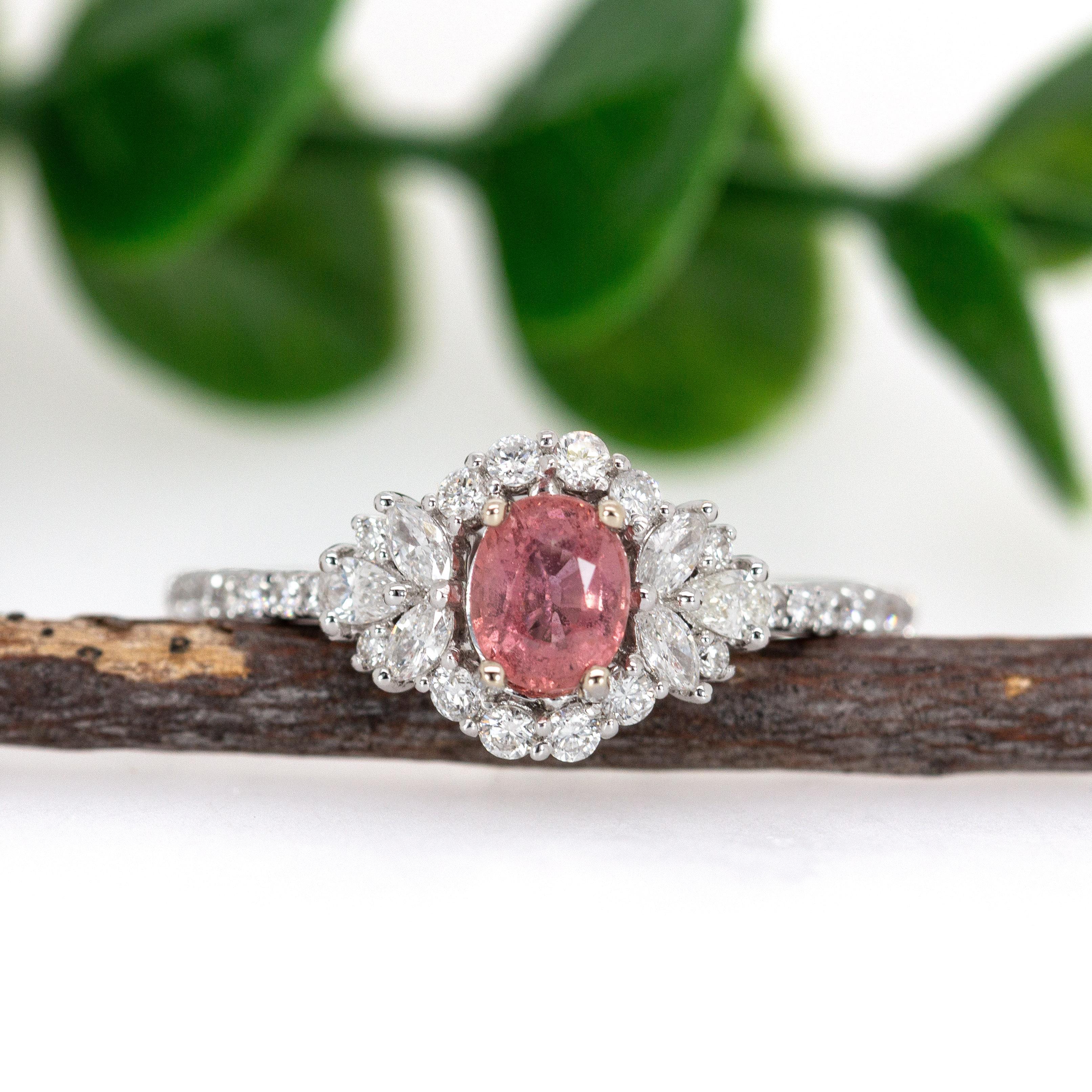 This is a 0.55-carat Padparadscha Sapphire and Diamond Ring set in 14K white gold. The centerpiece features a beautiful 5x4mm oval-shaped Padparadscha sapphire, which is known for its rare and distinct pink and orange color. The sapphire is
