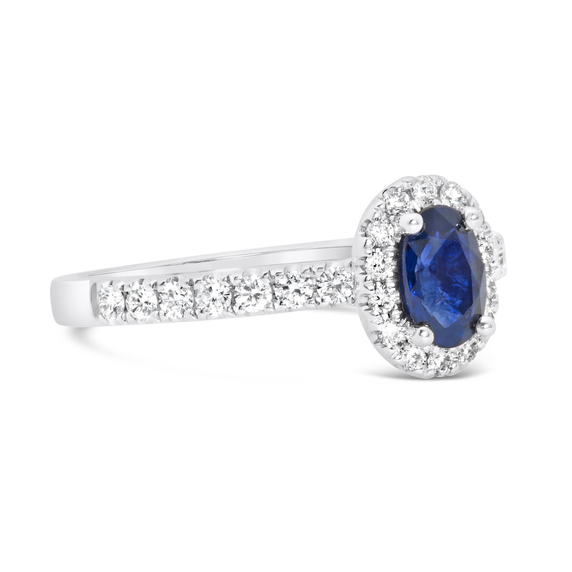 A gorgeous engagement ring, featuring a 0.56 carat oval cut blue sapphire, set on four rounded prongs. Surrounded by a halo of round brilliant cut diamonds and accented by a diamond encrusted shank on a half-eternity design. Diamonds weigh 0.33