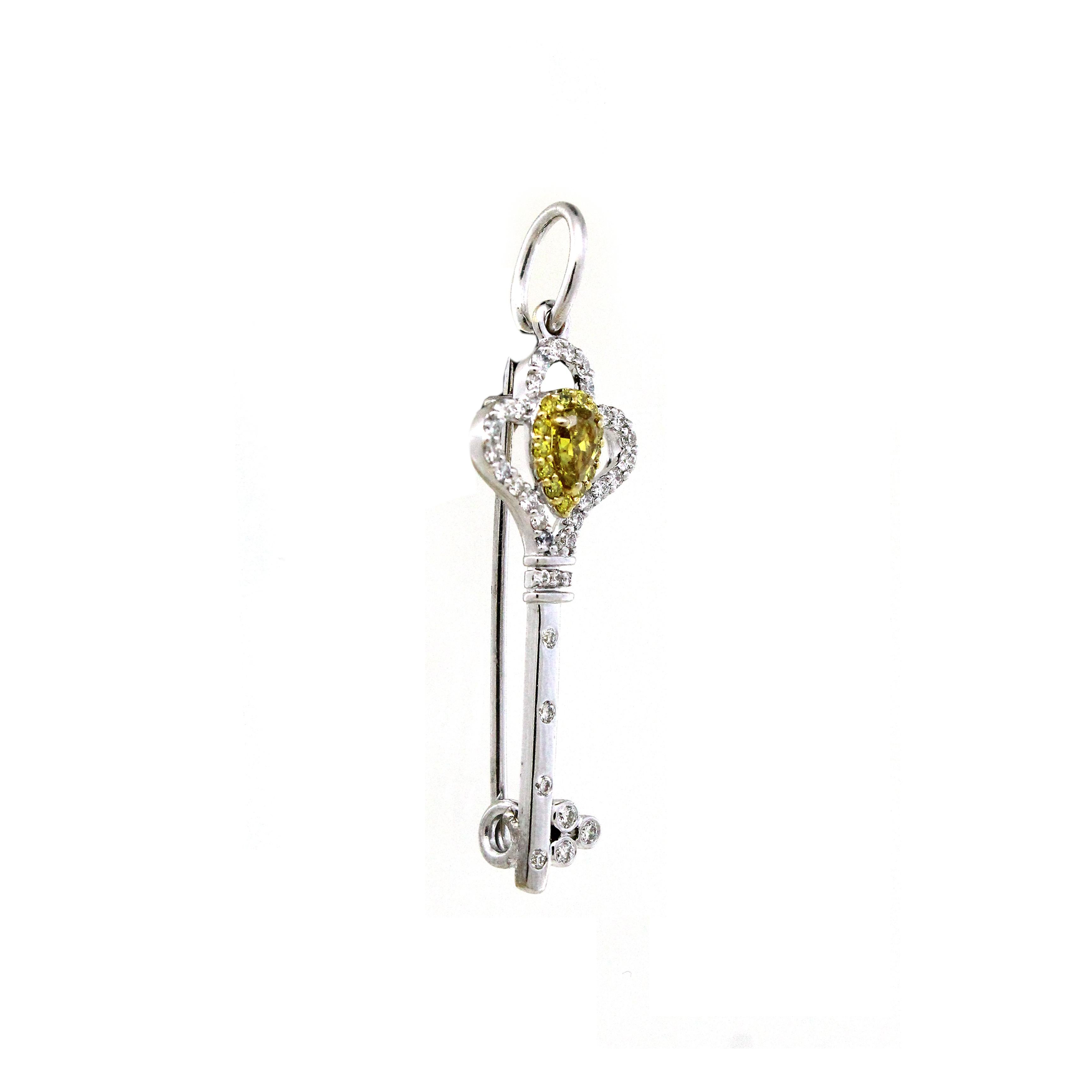 Questo elegante ciondolo unisex con spilla presenta una caratteristica silhouette a forma di chiave, realizzata in lussuoso oro bianco 18 carati e con un peso di 2,18 grammi. Al centro, uno splendido diamante giallo a forma di pera di 0,24 carati