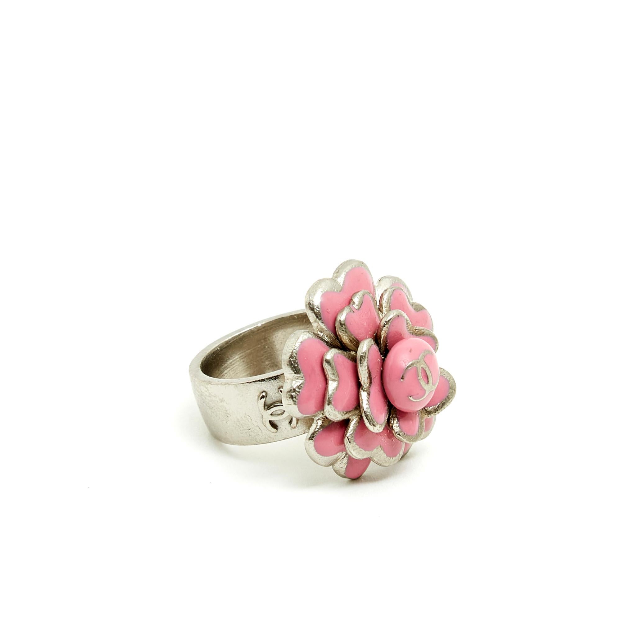 Chanel ring from the Cruise 2005 collection composed of a large ring and a camelia in silver metal and pink enamel surmounted by a CC. Finger circumference 53/54 approximately, inside diameter of the ring 1.72 cm, width of the ring 0.8 cm, diameter