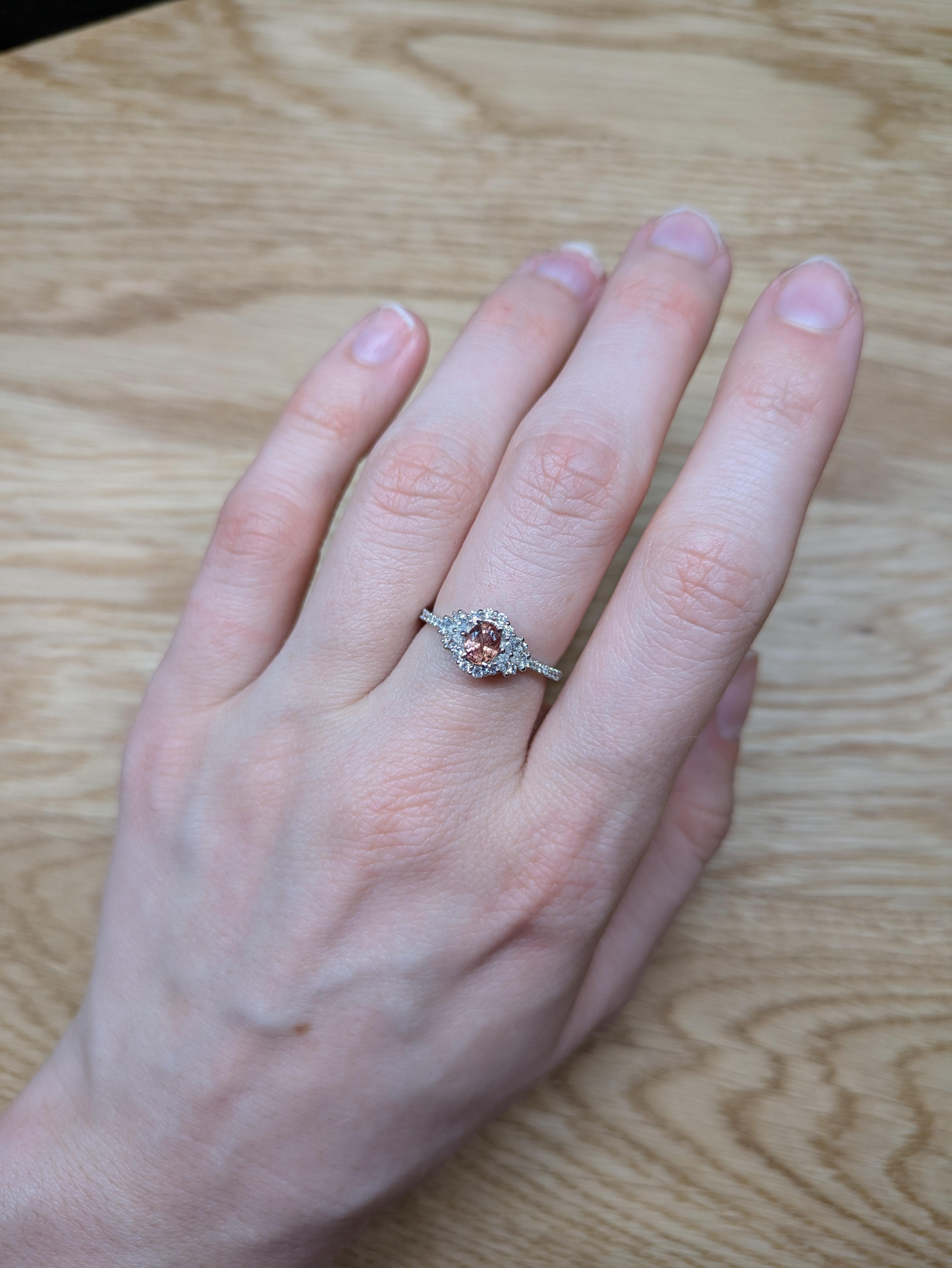 Delicadamente elaborado en oro macizo de 14 quilates, este exquisito anillo incorpora un raro zafiro Padparadscha ovalado de 0,5 ct (5x4 mm), conocido por su cautivadora mezcla de tonos rosa y naranja. Acentuada con diamantes naturales, ofrece una