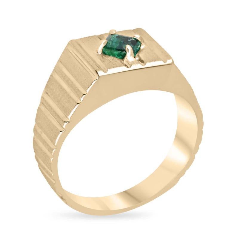 This striking men's solitaire ring showcases a AAA-quality Zambian emerald with a rich dark green color, expertly cut in a classic emerald shape. The gemstone is set in four prongs but offset for a unique and modern twist, making this ring stand out