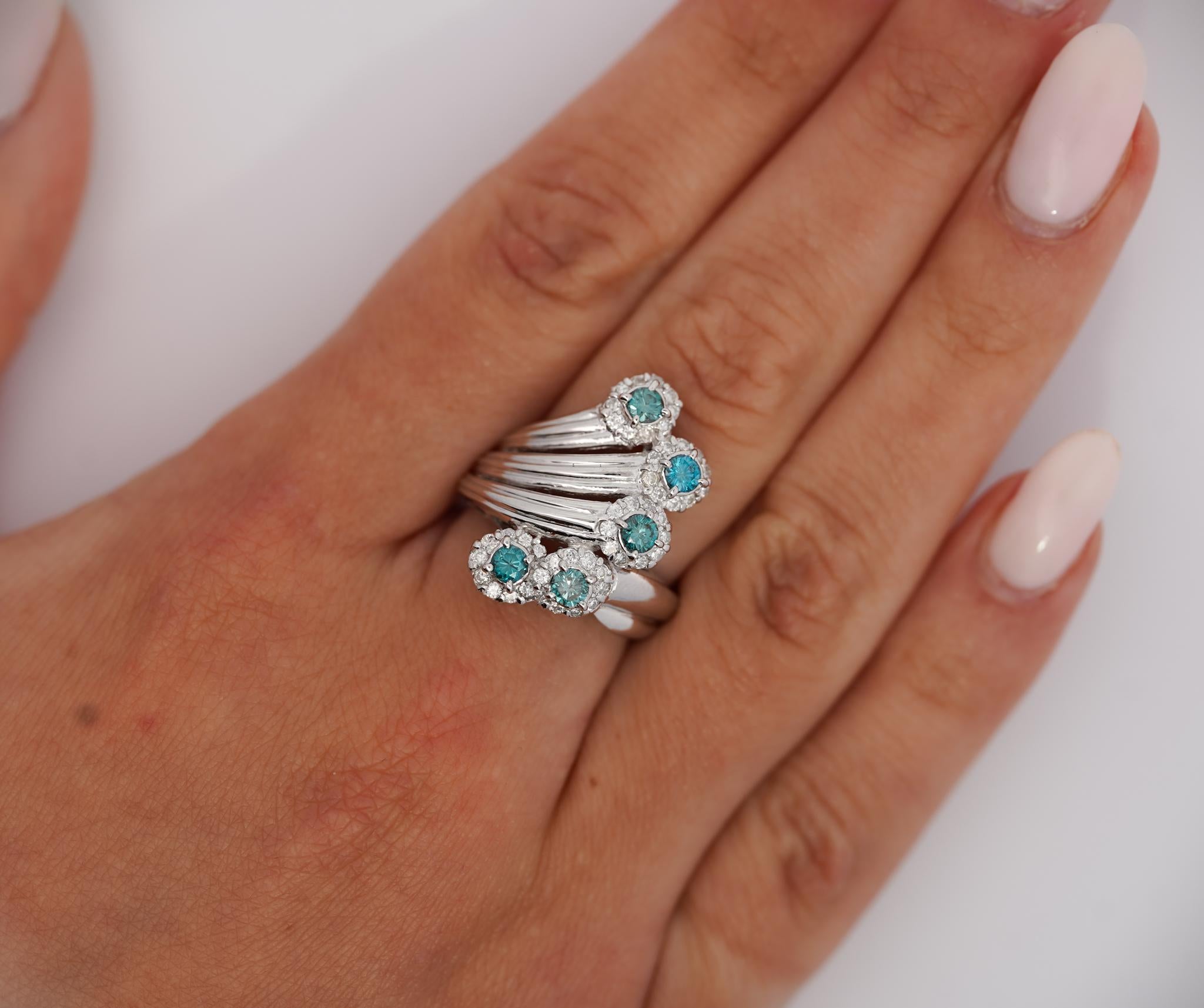 Anello in platino con diamante blu e diamante bianco taglio rotondo. 

Questo anello dal design intricato presenta una struttura a più bande che gli conferisce un aspetto stratificato. Presenta diversi grappoli di gemme, ciascuno con un diamante blu