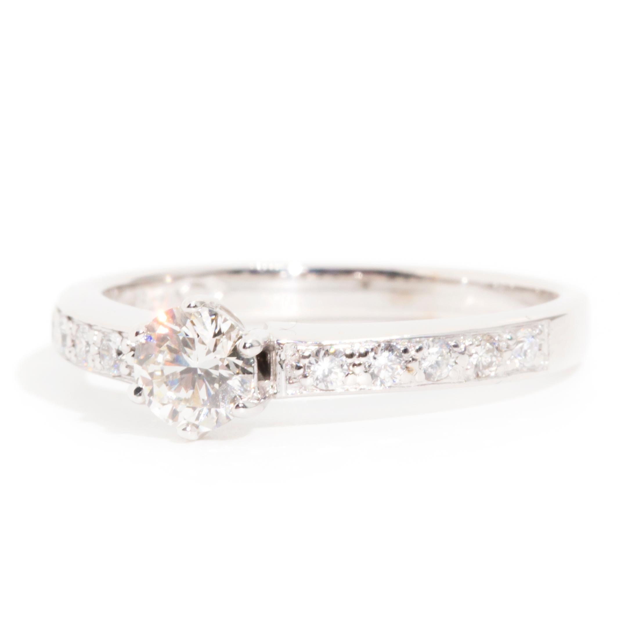 Lovingly forged in 18 carat white gold, this opulent vintage engagement ring features an impressive 0.45 carat round brilliant cut diamond raised up from an elegant band in a six claw setting, flanked by glittering rows of round brilliant diamonds.